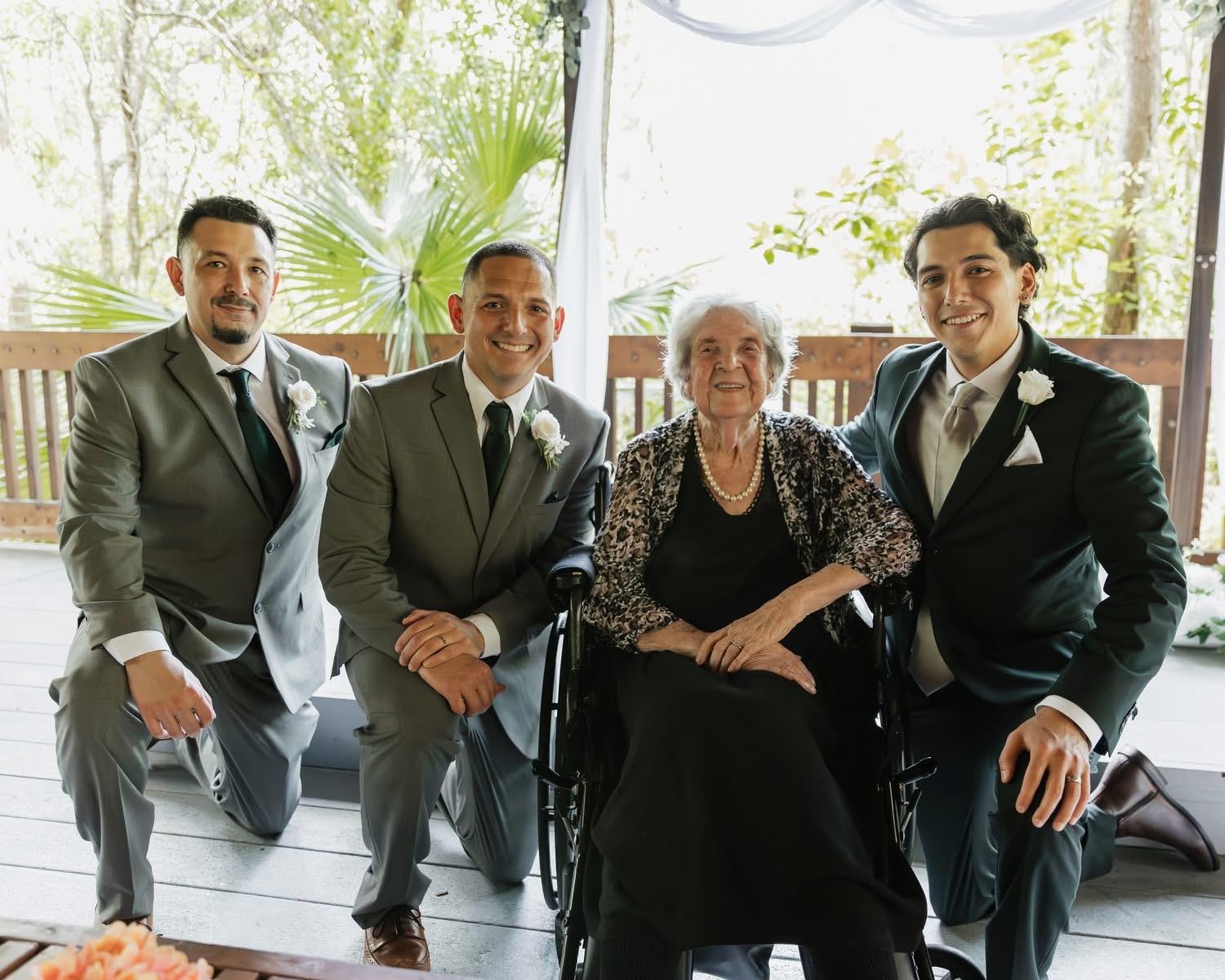 Four men smile around a woman in a wheelchair at a family celebration in a garden.