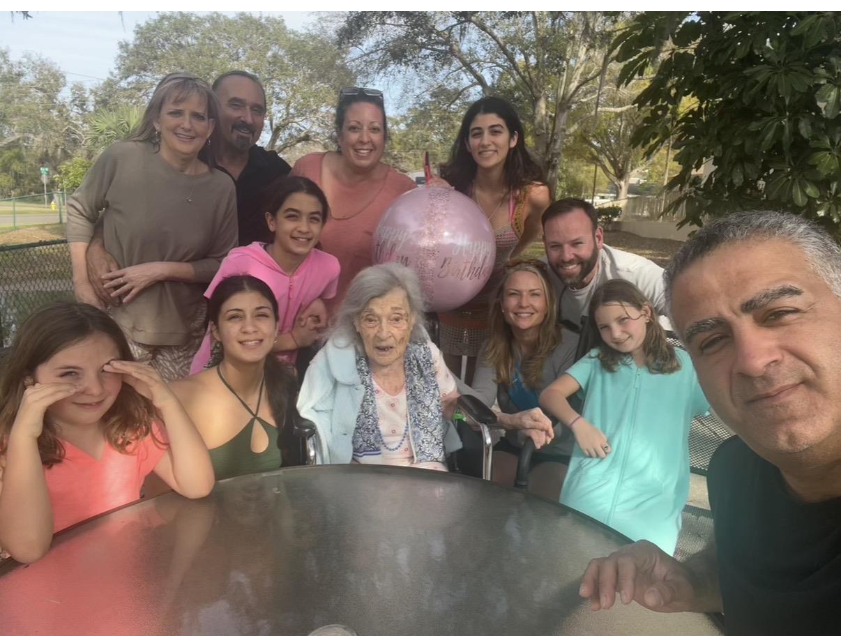 A large group of family members enjoys a gathering in the park with a pink balloon.