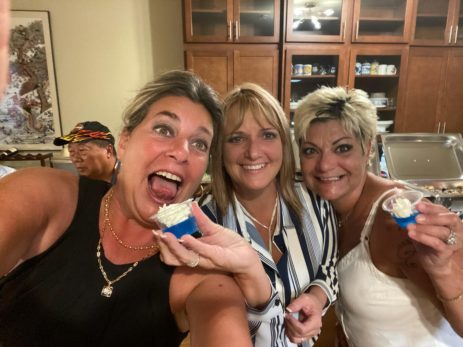 Women celebrate and eat cupcakes together in a cozy kitchen setting at night.