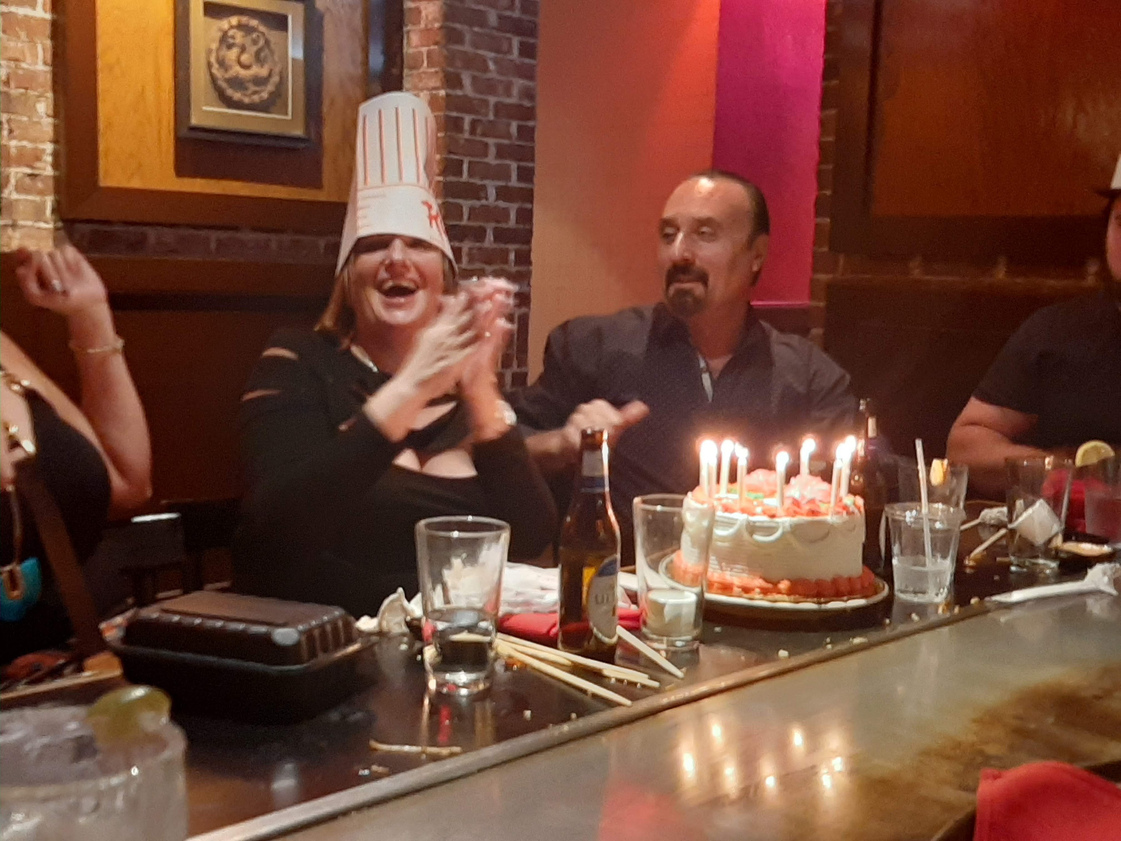 People are enjoying a celebration with a cake and candles in a lively restaurant setting.
