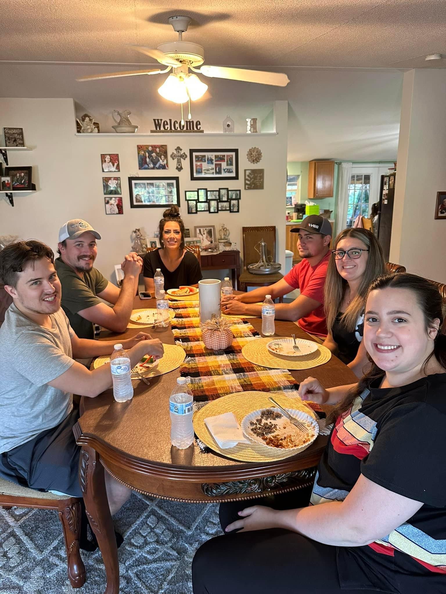 Six friends sit together at a dining table, eating and laughing. They enjoy food and drinks.