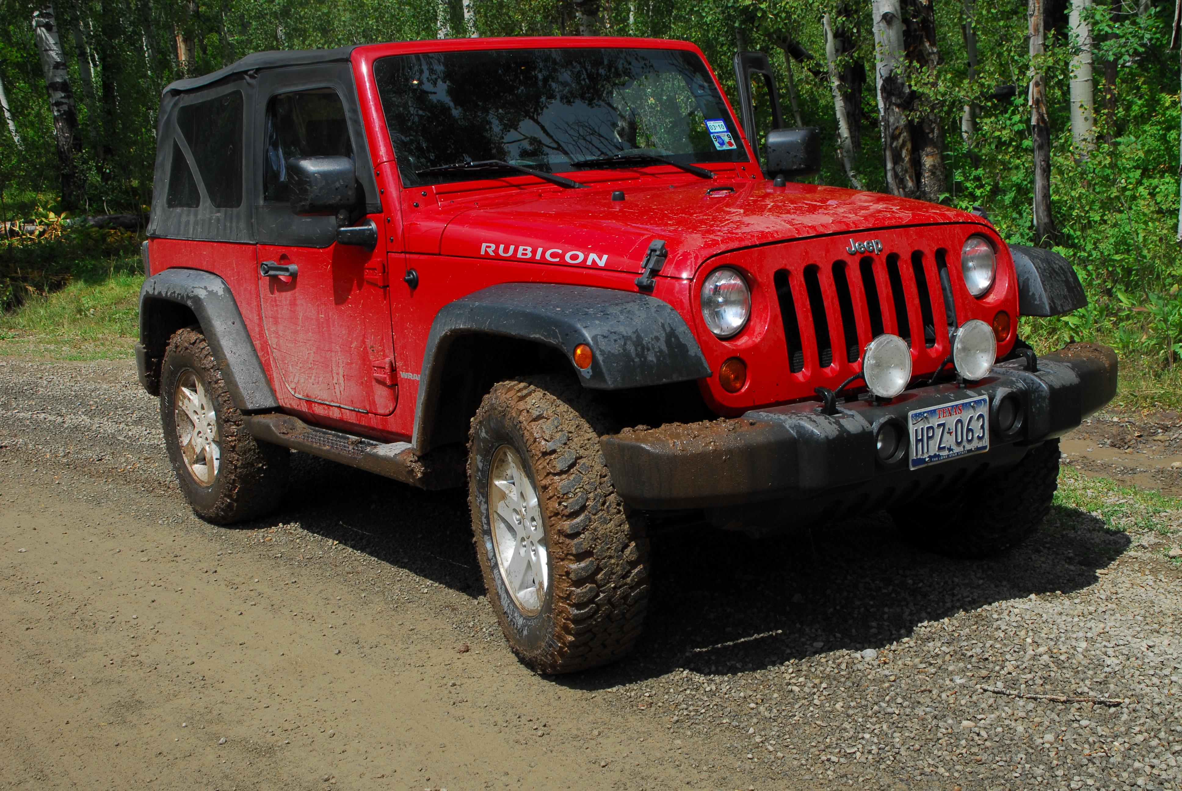 A red Jeep Rubicon is parked on a dirt road surrounded by trees in the forest during the day.