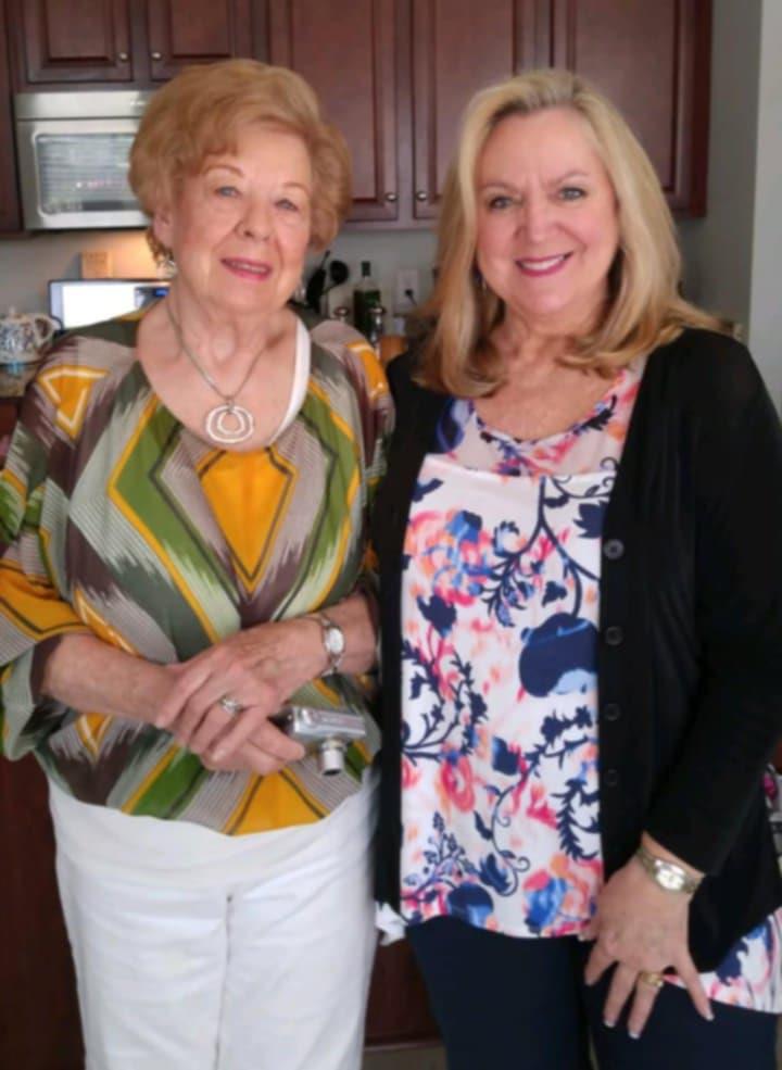 Two women stand side by side in a kitchen, sharing smiles during a family get-together.