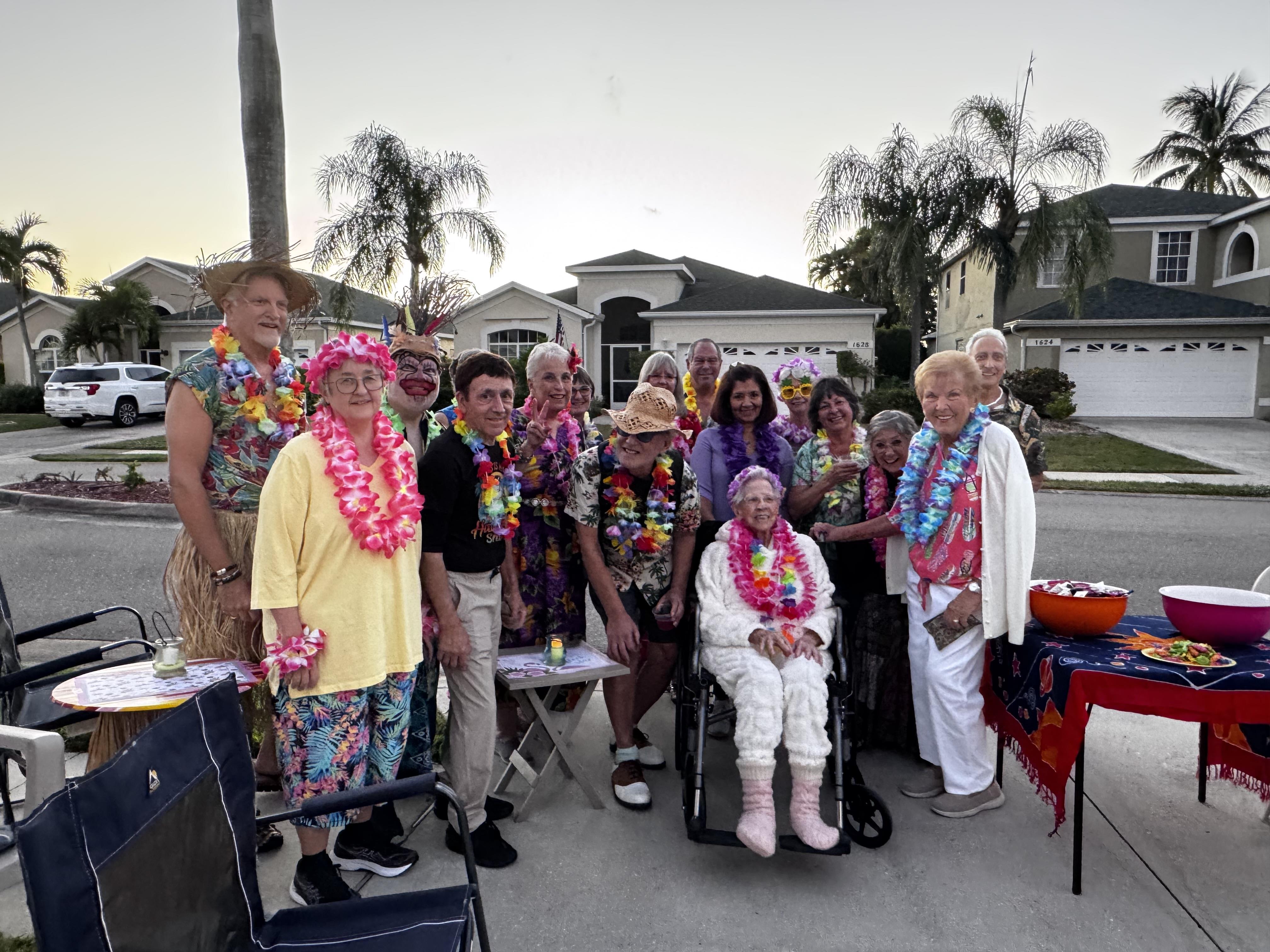 People stand together wearing colorful outfits and leis for a celebration in a suburban area.