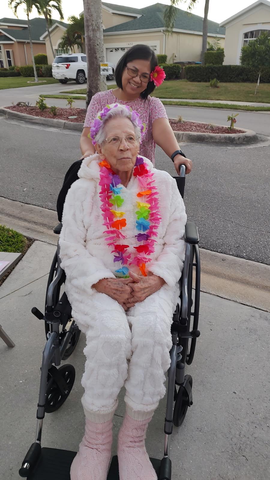 An elderly woman sits in a wheelchair at an outdoor event with bright decorations.