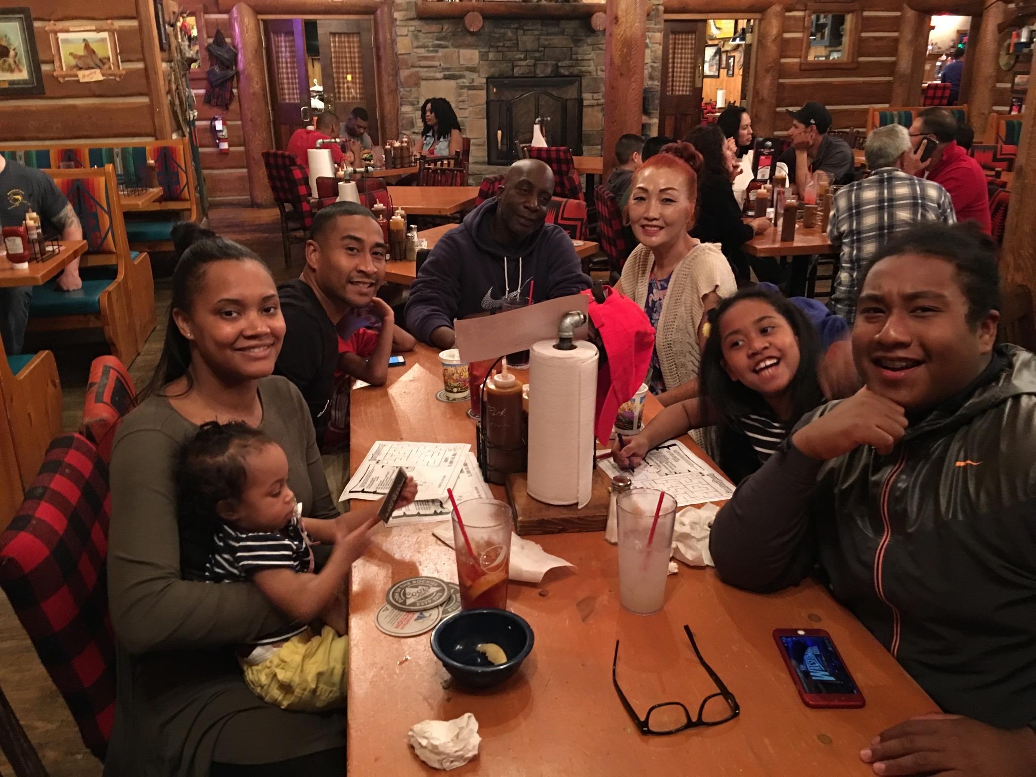 A group of family members gathers around a table for dinner in a busy restaurant.