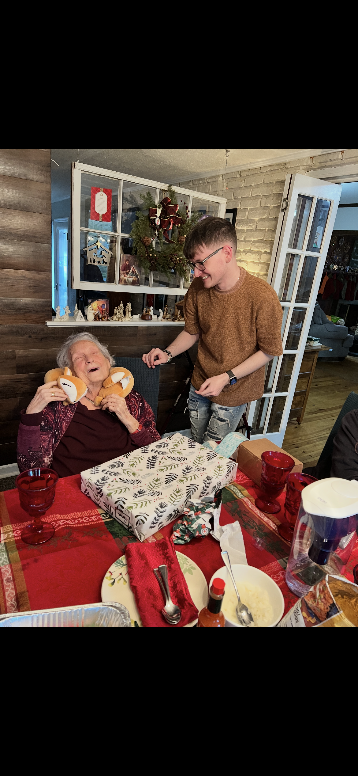 A young person gifts a smiling older woman stuffed toys at a family event.