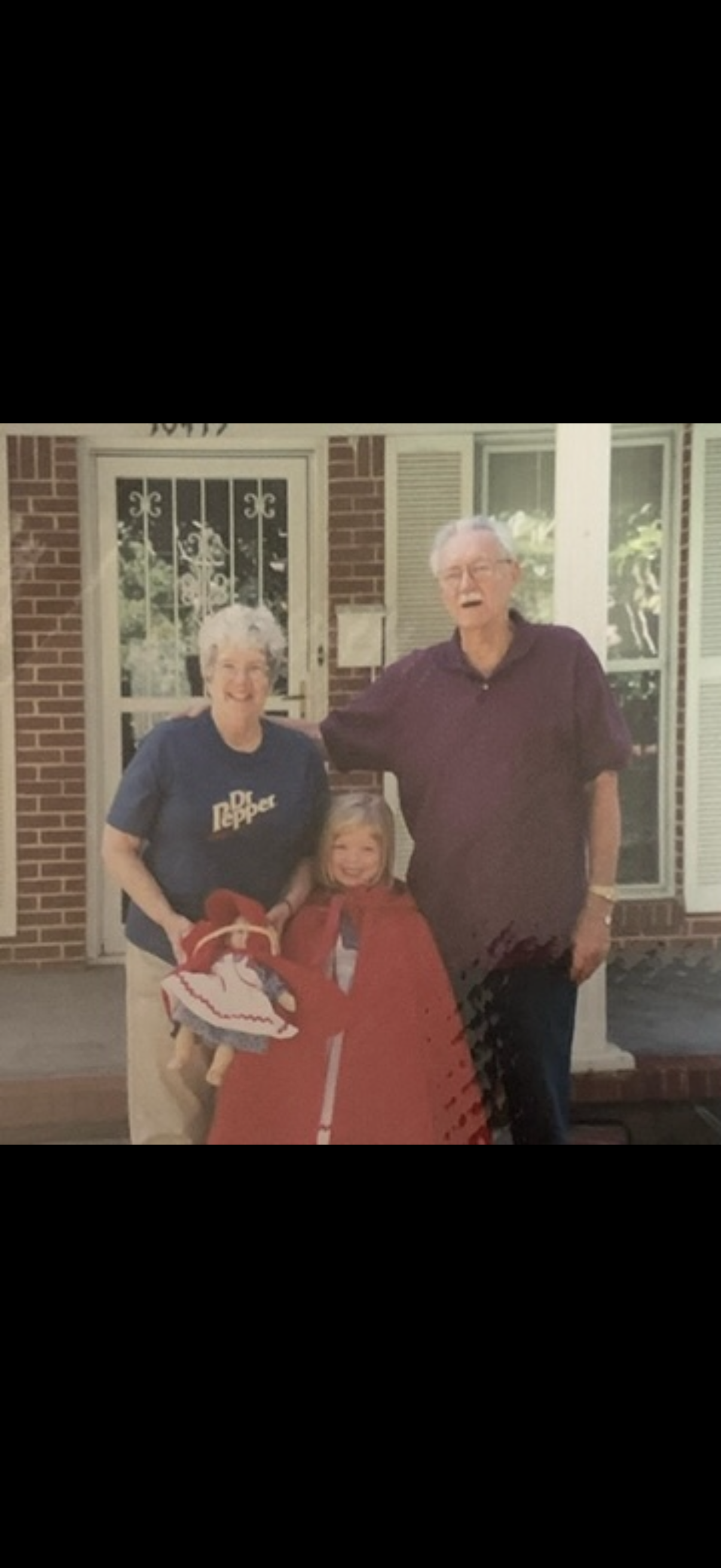 Three people pose outside a brick house wearing casual clothes and smiling for the camera.