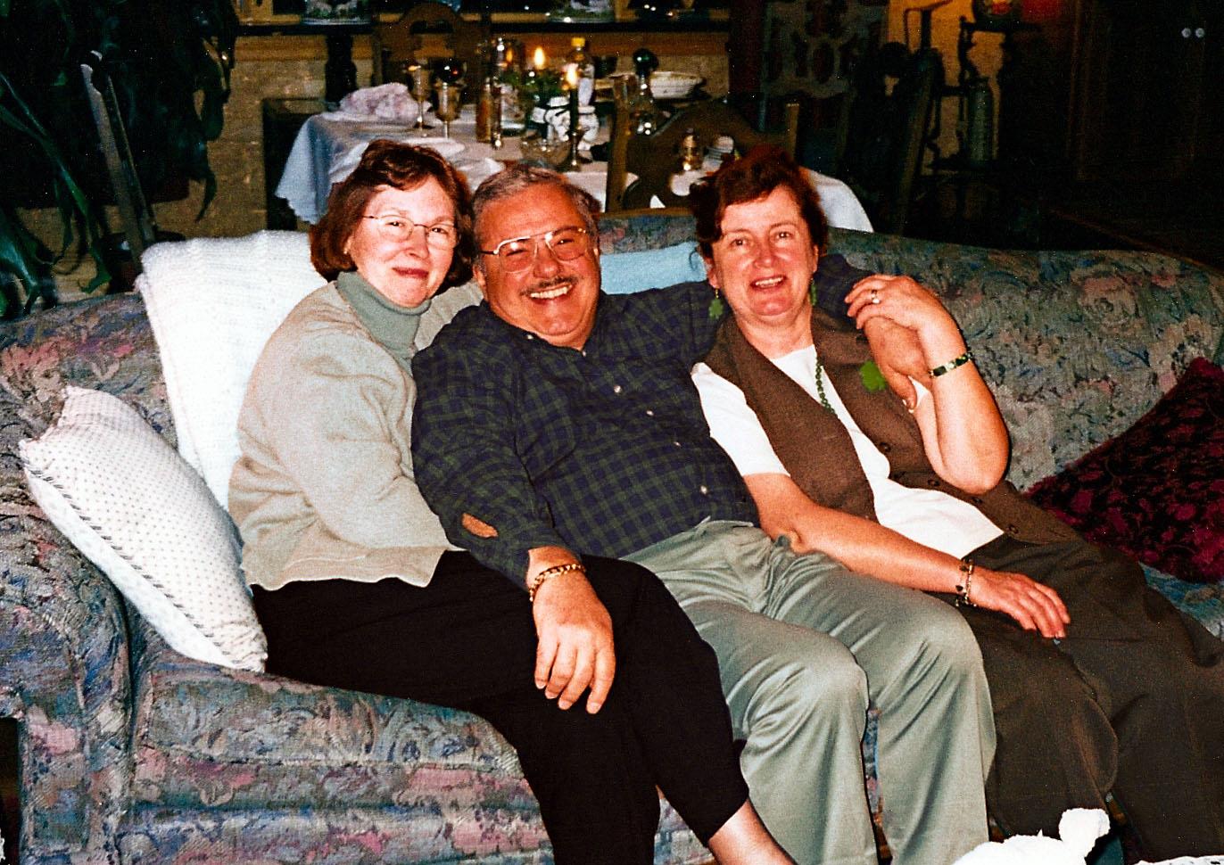 Three people enjoy each other's company while sitting on a couch in a social setting.