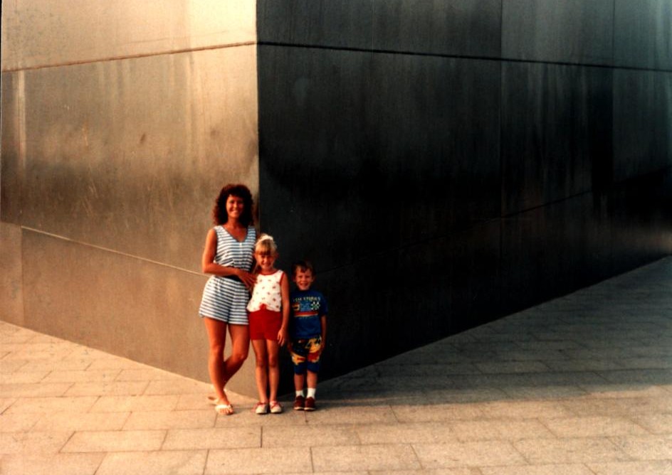 Three people enjoy an outdoor moment near a large metal structure during sunset in a city park.