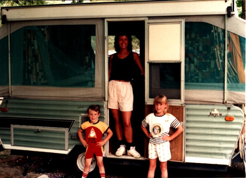 A family enjoys time together outside their camping trailer during a summer day.