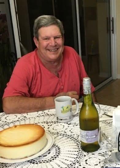 A man sitting at a table with a cheesecake and a bottle of wine