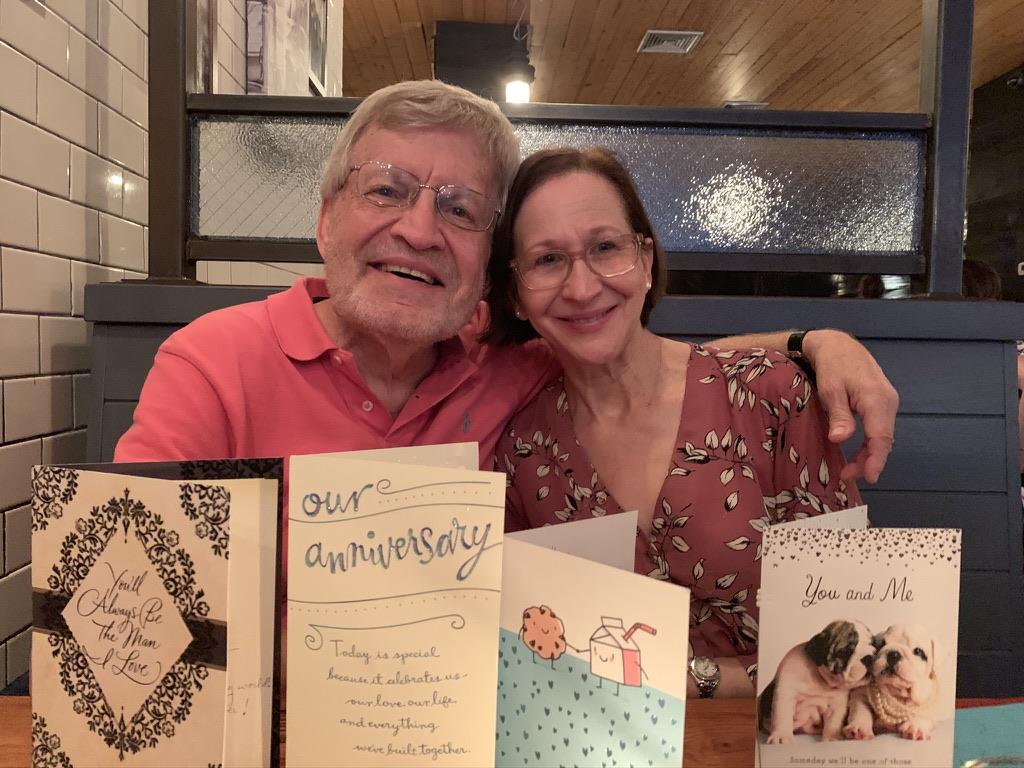 A couple sits together at a table with anniversary cards, smiling and enjoying their time.