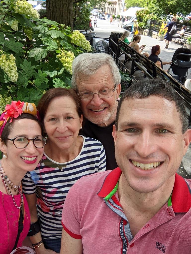 Four friends pose happily while enjoying a day outdoors among flowers in a park.
