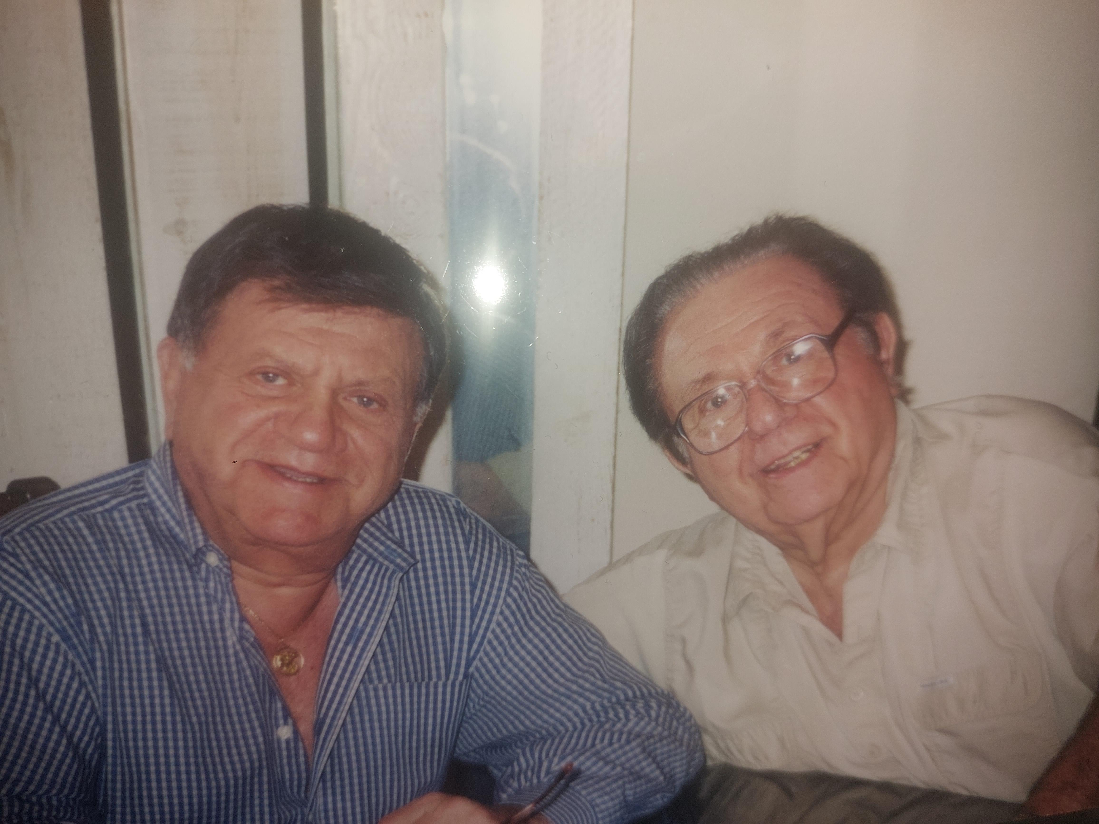 Two men sit next to each other and smile while enjoying a moment together in a relaxed setting.