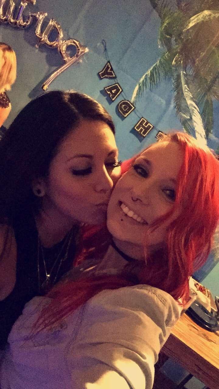 Two friends smile and take a selfie together at a social event in a lively setting.