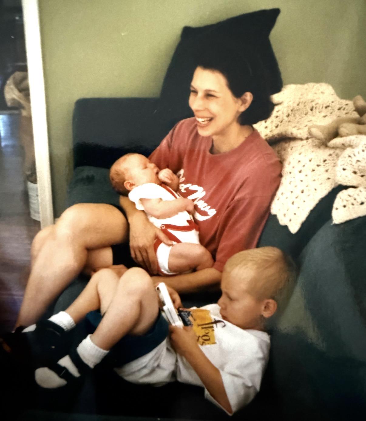 A woman holding a baby and a baby sitting on a couch