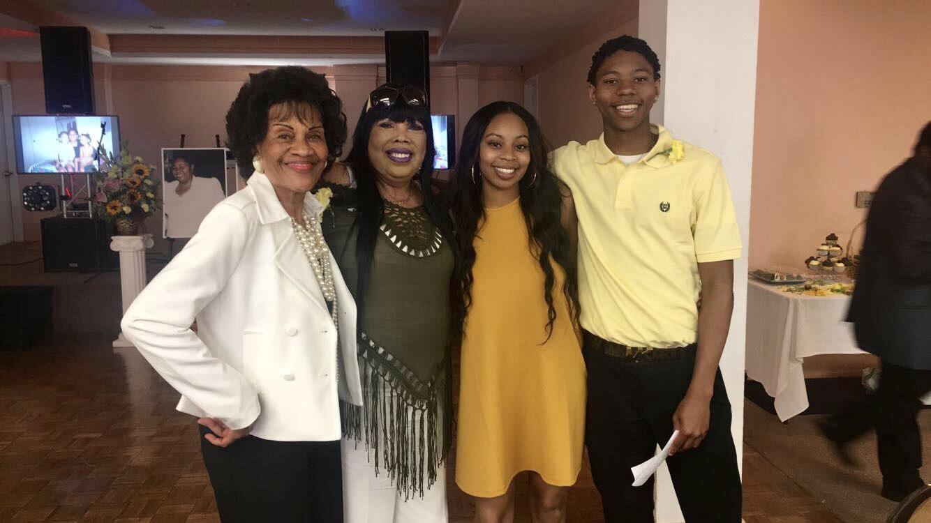 Four people are standing together and smiling during a social event in the evening.