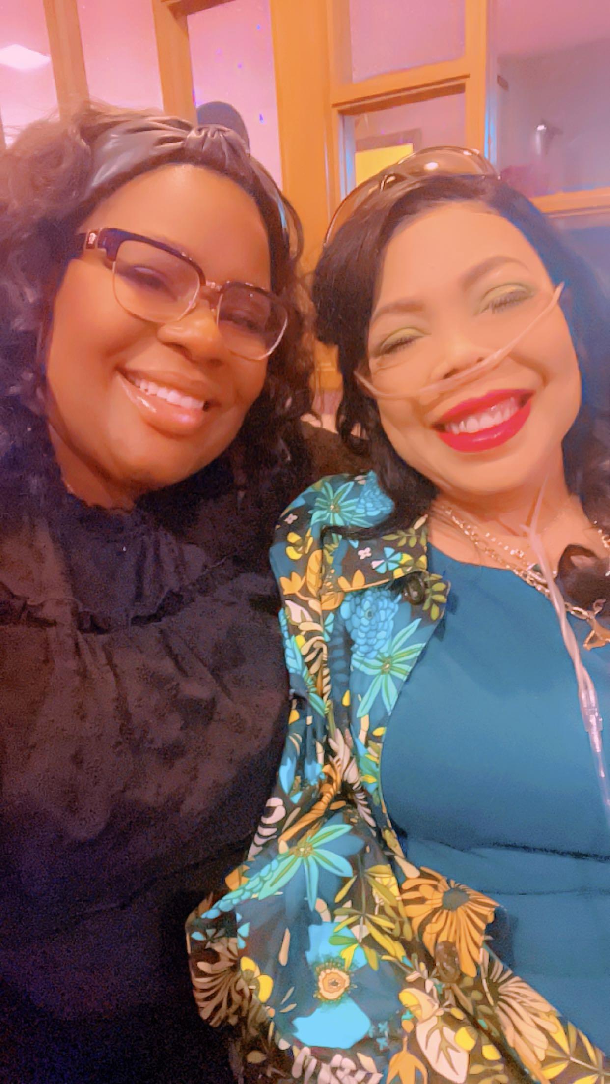 Two women are smiling and posing for a picture at an event with colorful decorations around.