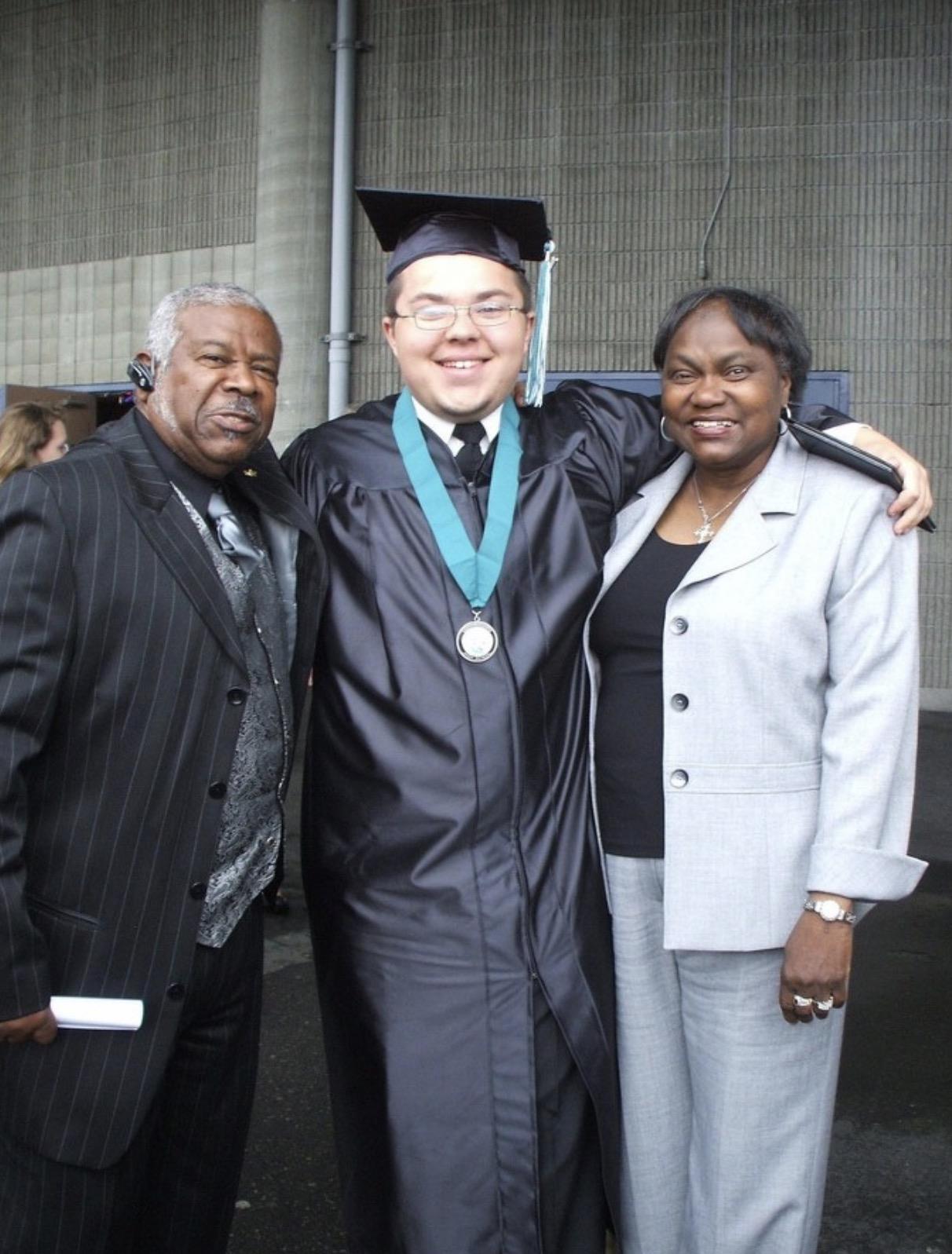 Two family members stand next to a graduate in a cap and gown during a ceremony event.