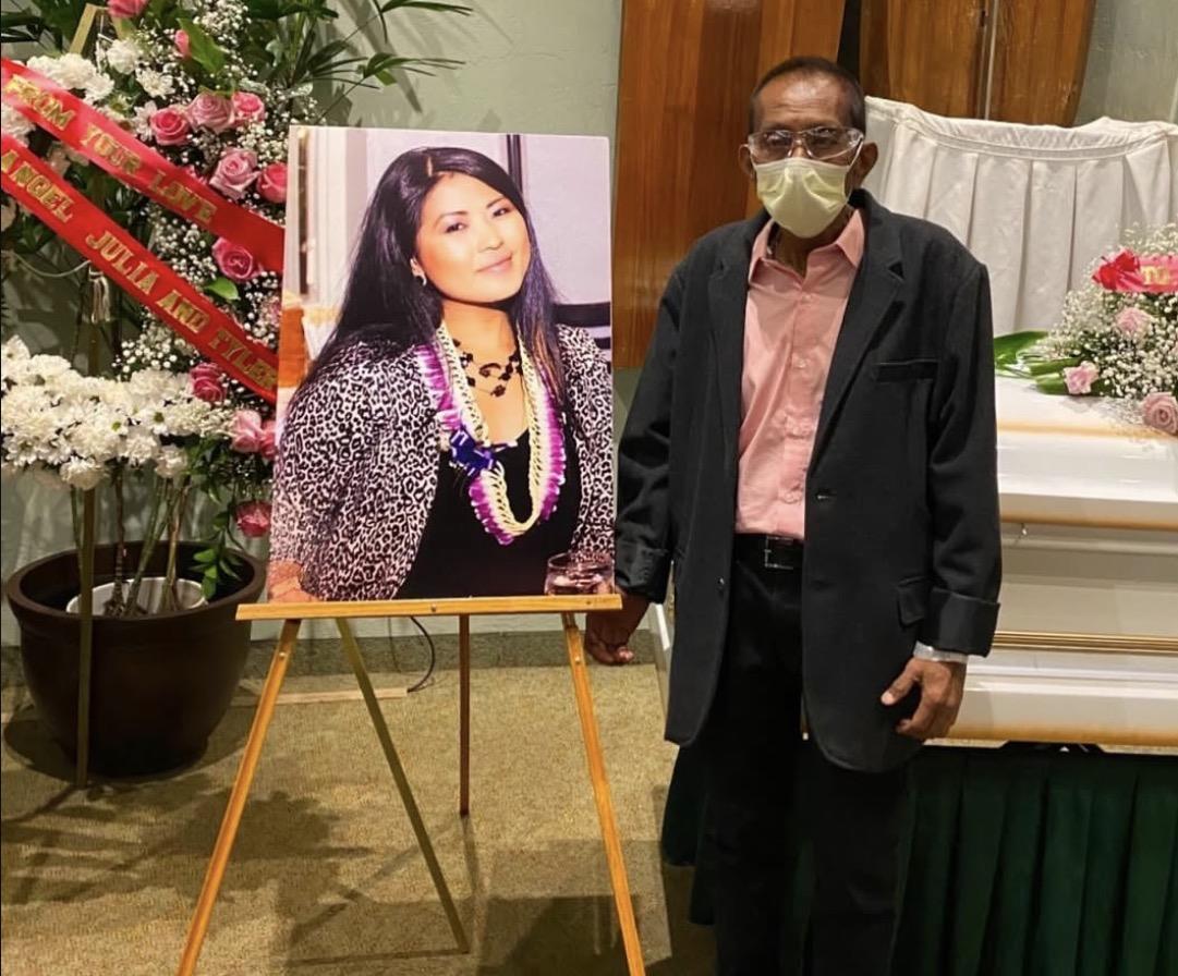 A man stands near a portrait at a memorial service in a church hall during the evening.