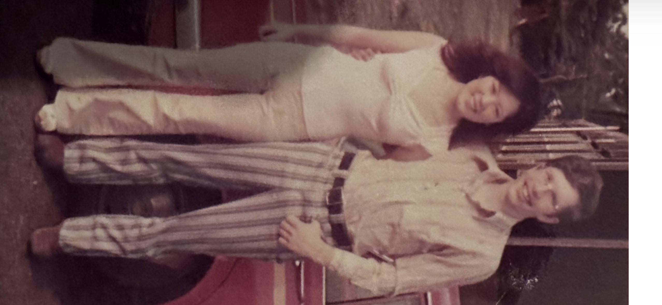 Two people smile together outdoors in casual clothes amid a bright setting.