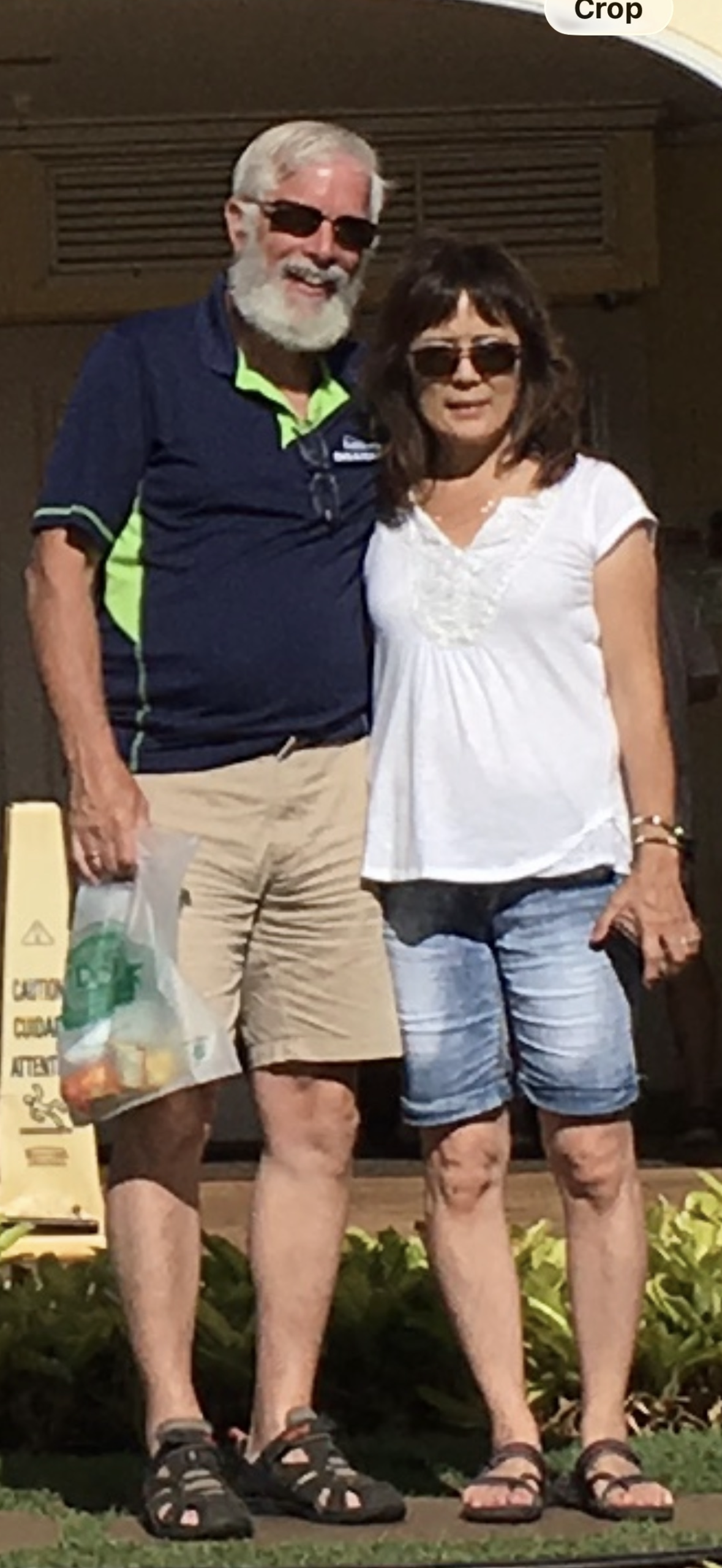 A couple stands closely together outside a store holding a bag filled with food items.