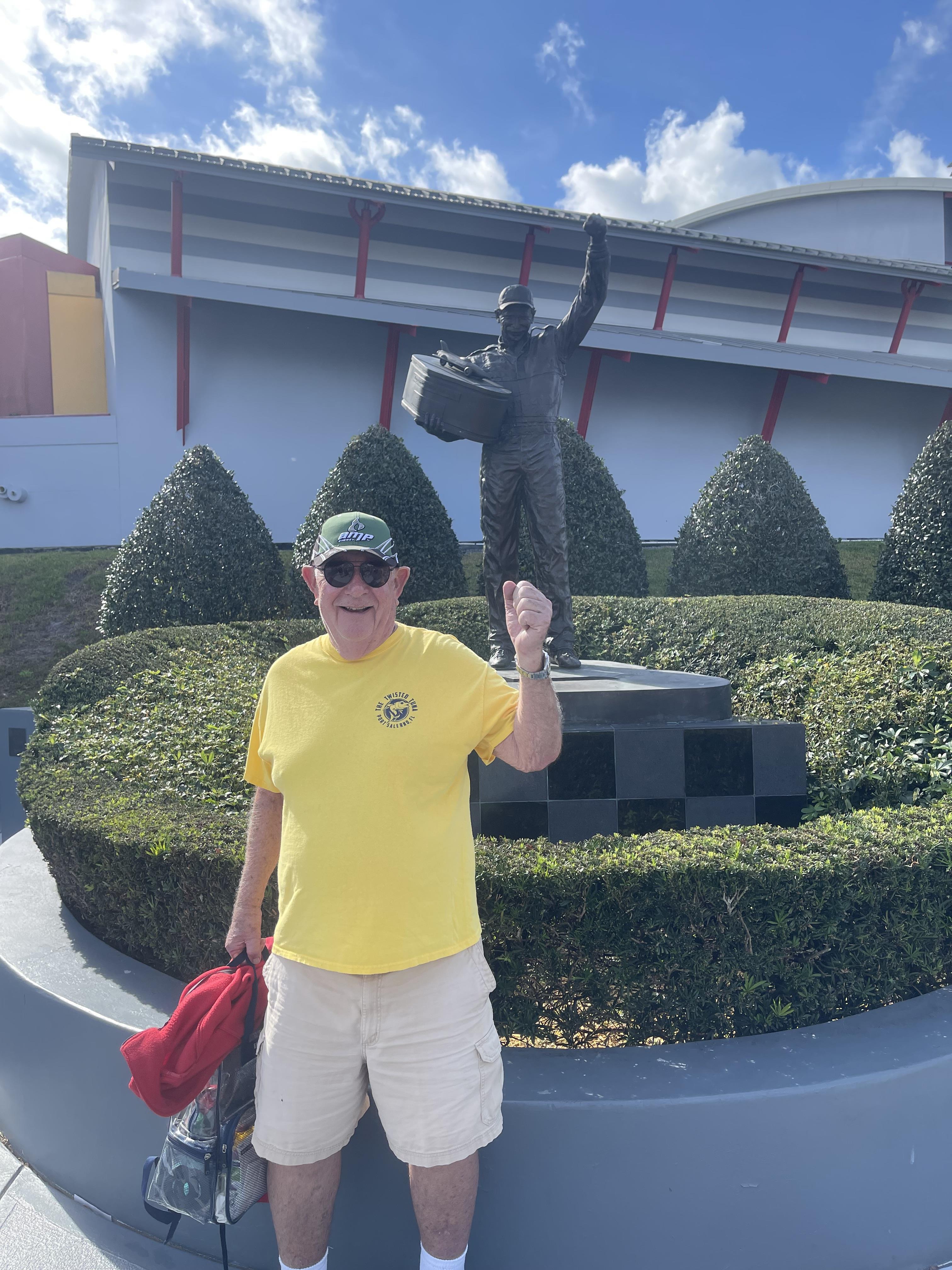 A man in a yellow shirt and white shorts holding a suitcase in front of a statue