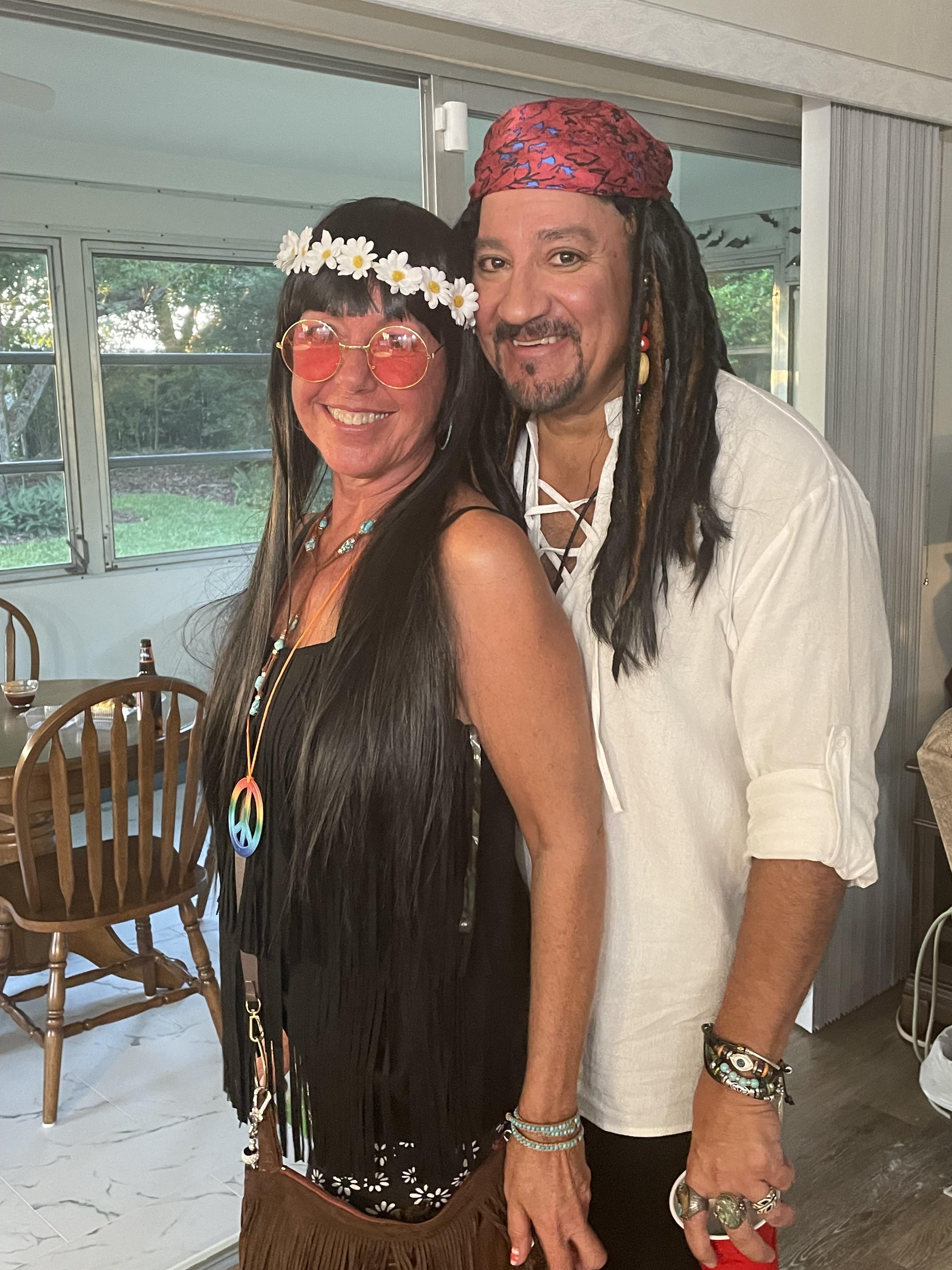 Two people stand together in a living room, both wearing costumes for a party.