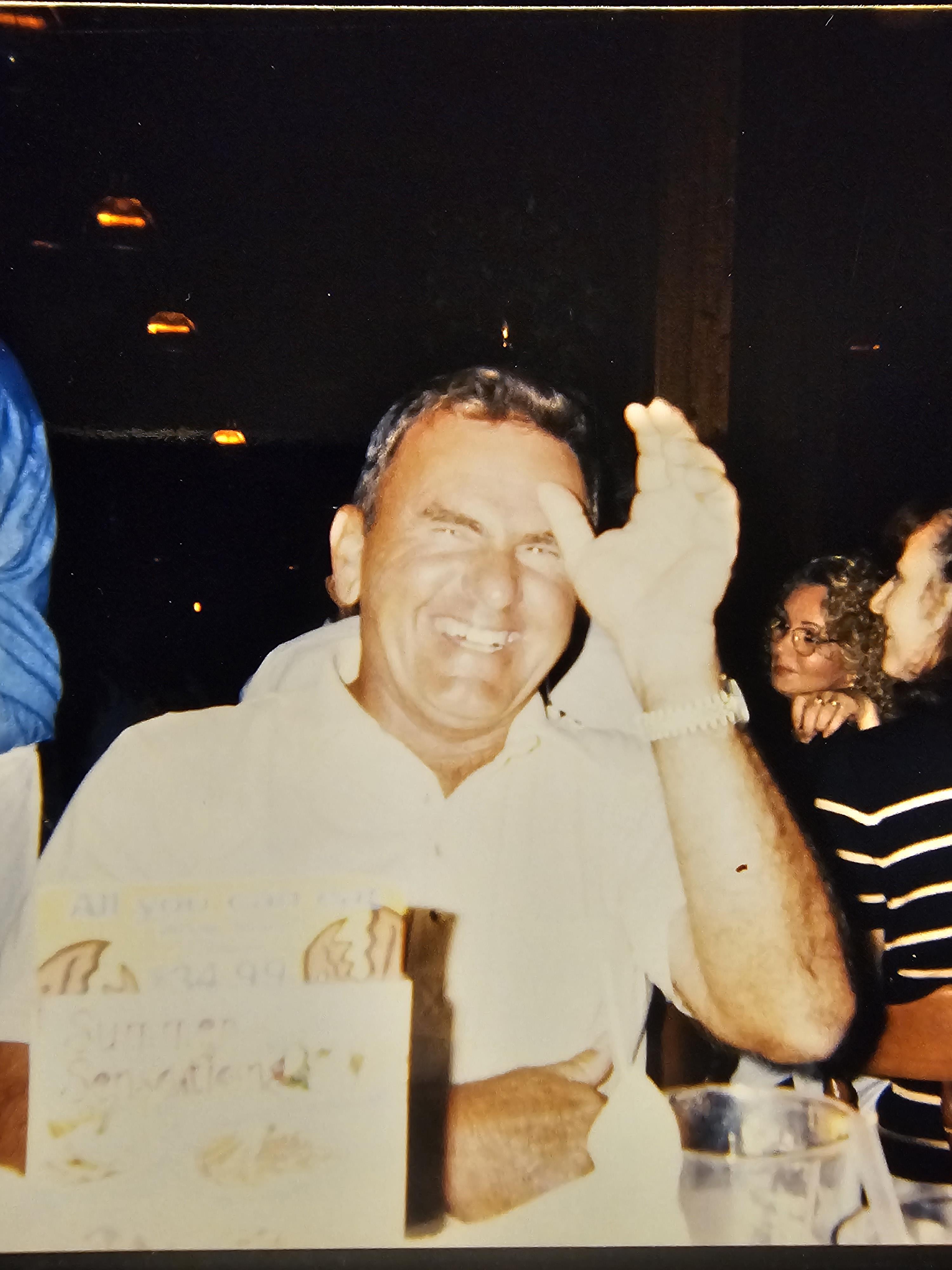 A man laughs and waves his hand while sitting at a table during a gathering with friends.
