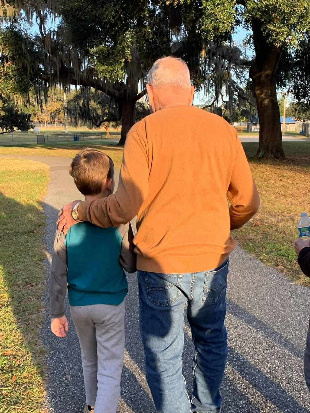 A grandfather and grandson are walking on a path surrounded by trees.
