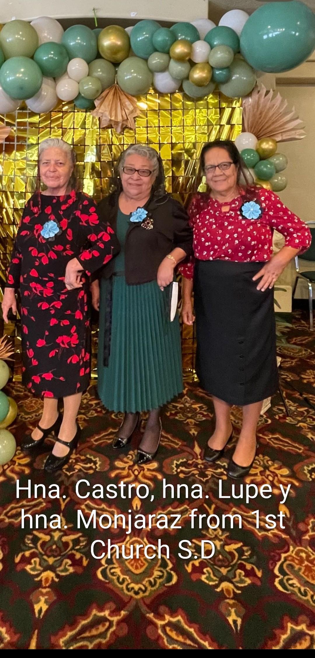 Five women smile in varied outfits at a special event decorated around them.