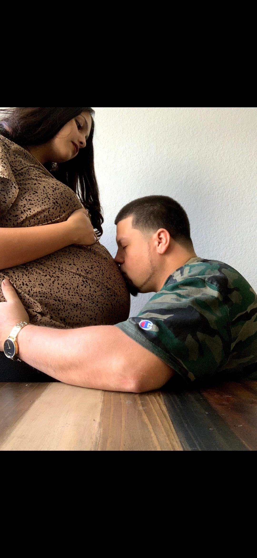 A man kisses a pregnant woman's belly while they sit on a wooden floor in a private space.