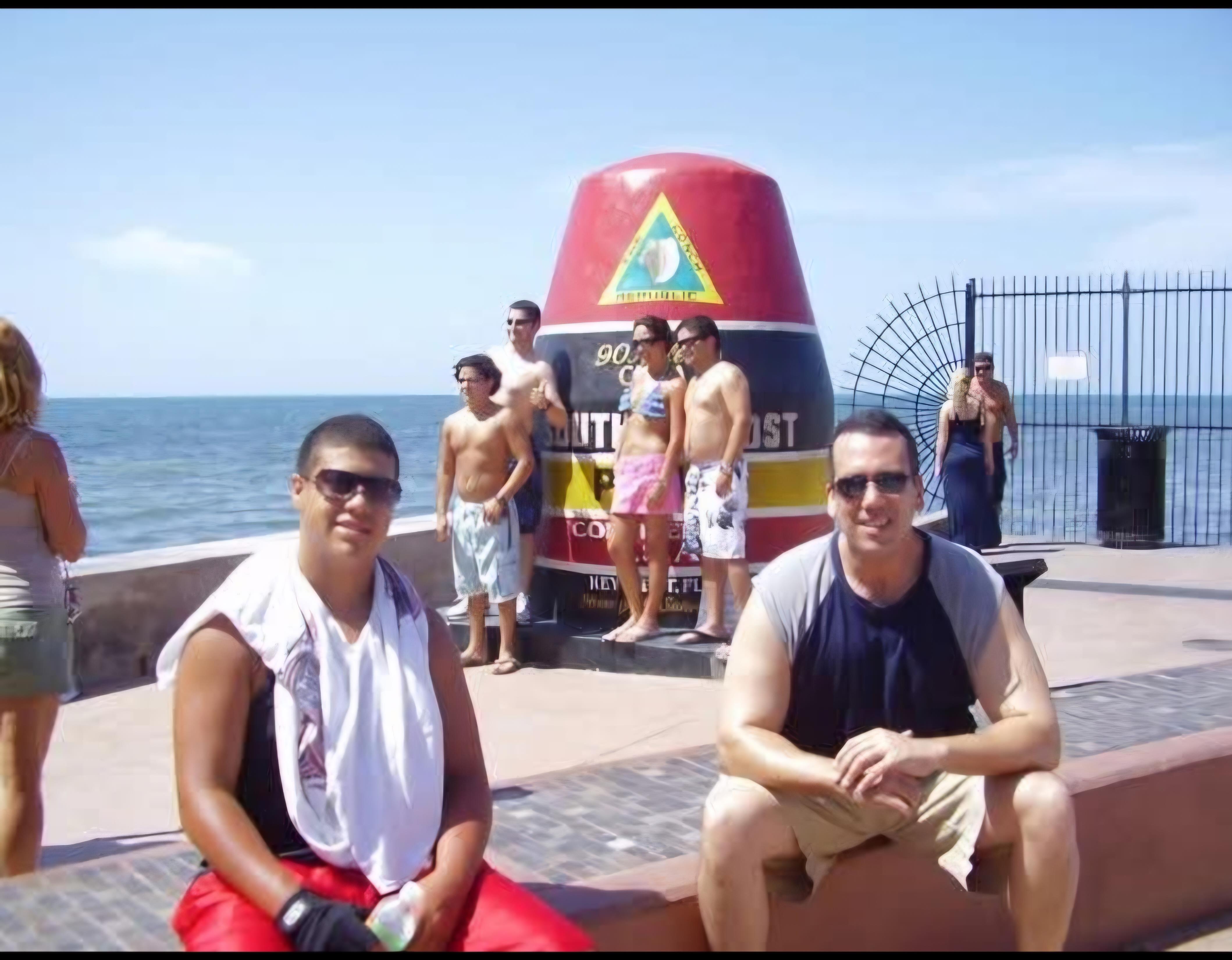 Friends gather near a large buoy by the ocean, enjoying a warm summer day at the beach.