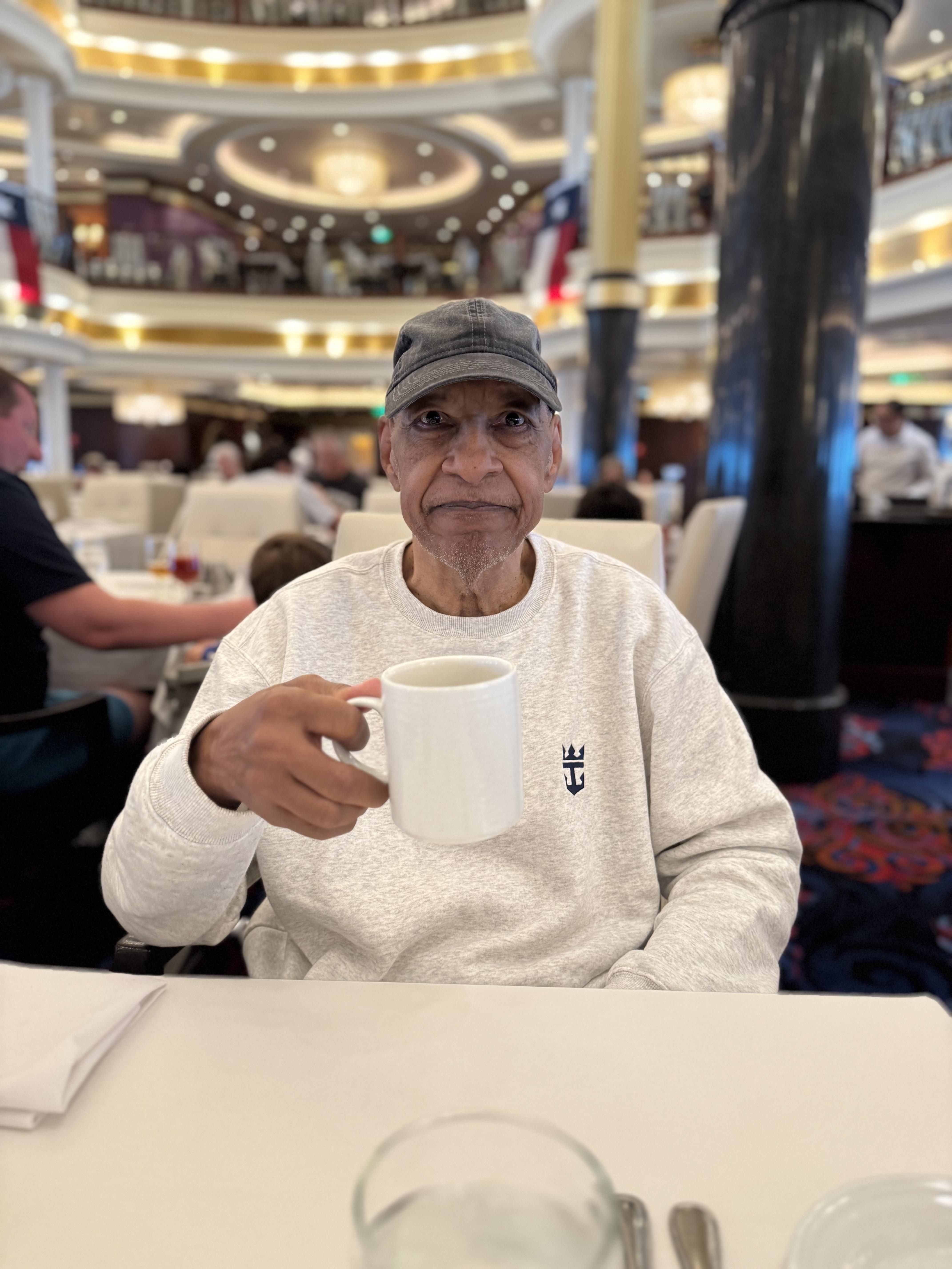 An elderly man enjoys his morning coffee at a dining table on a cruise ship.