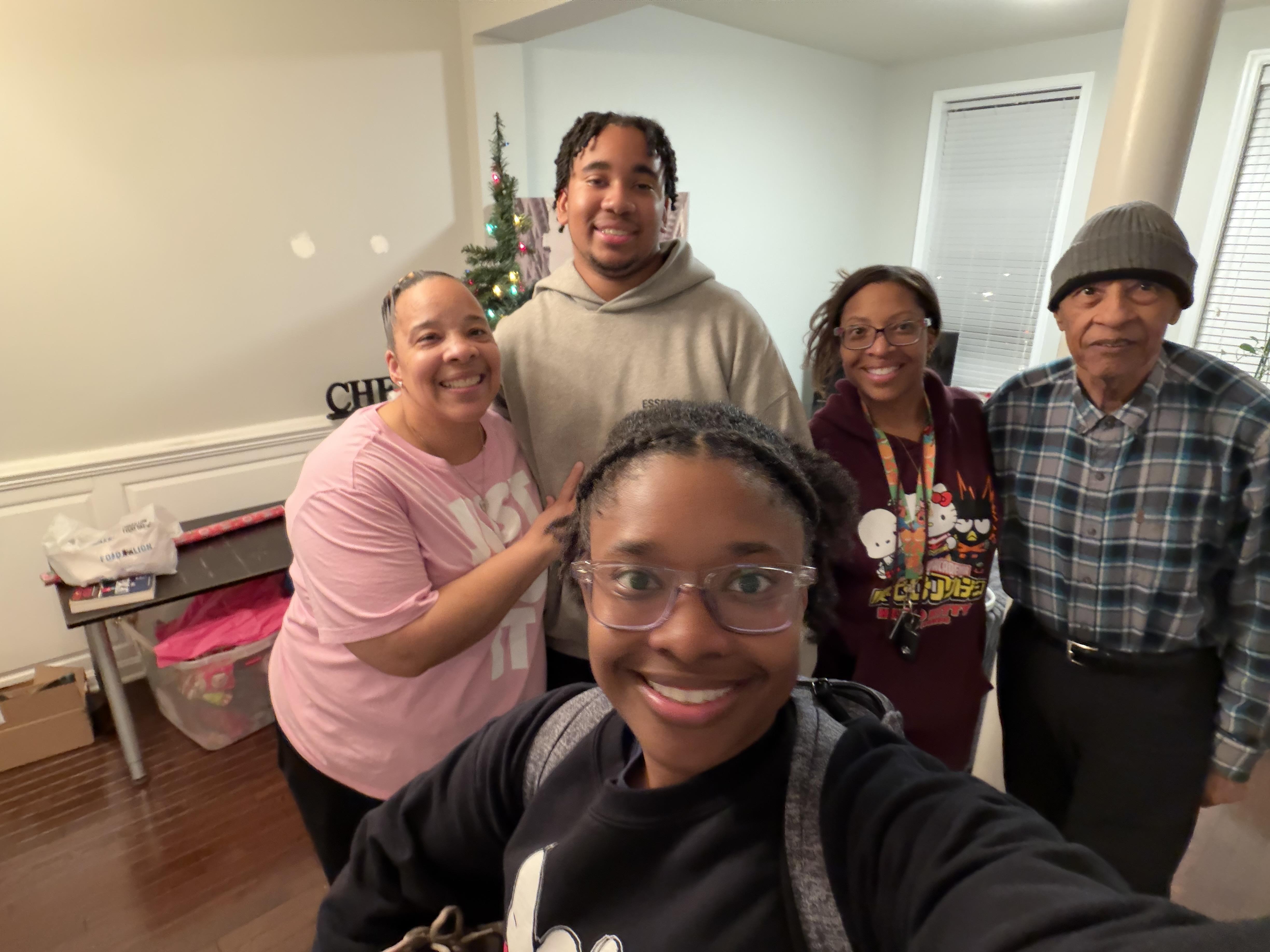 A group of five people stands together smiling in a living room decorated for the holidays.