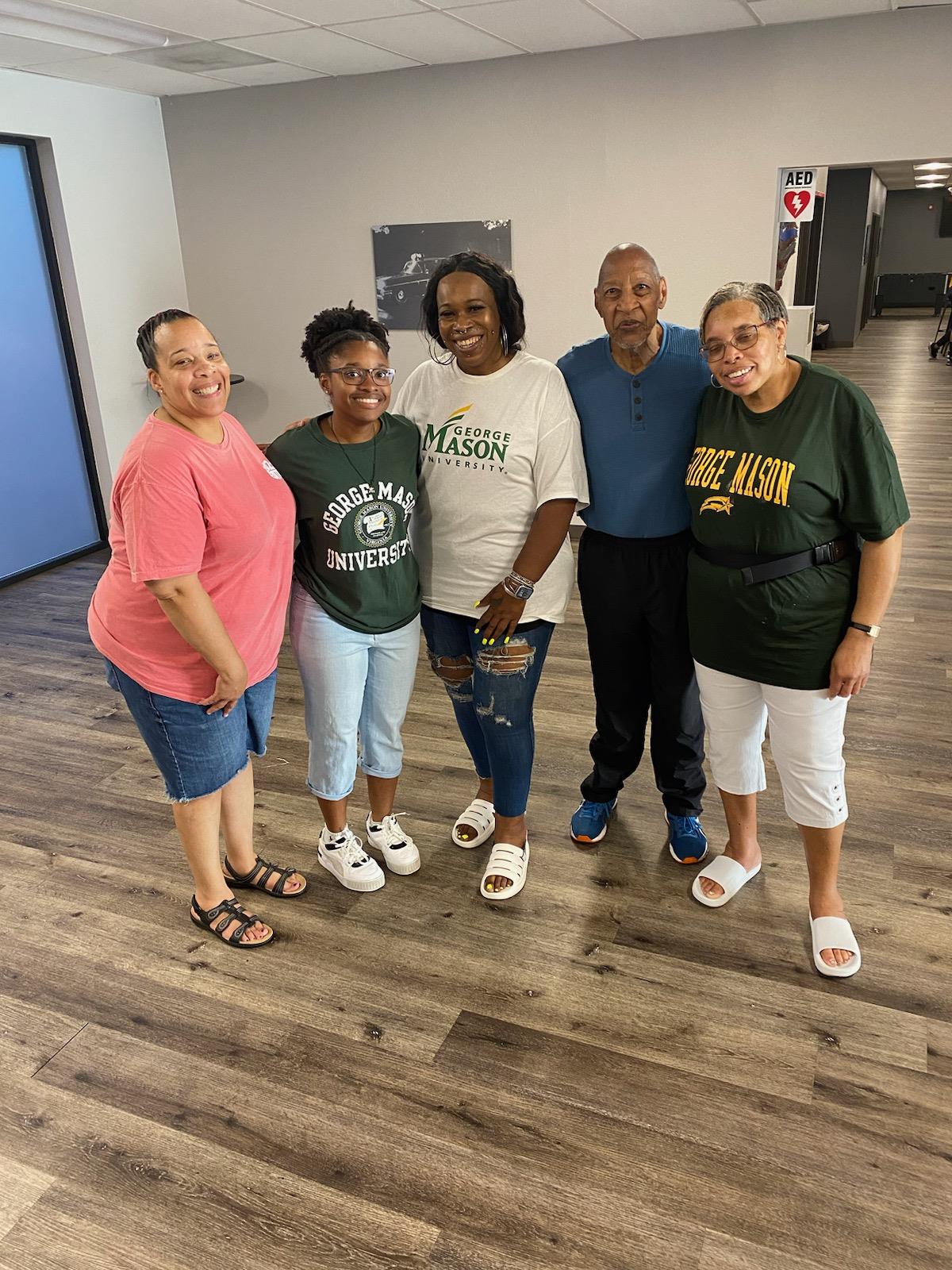 Five friends stand together smiling in a community center. They are having a reunion.