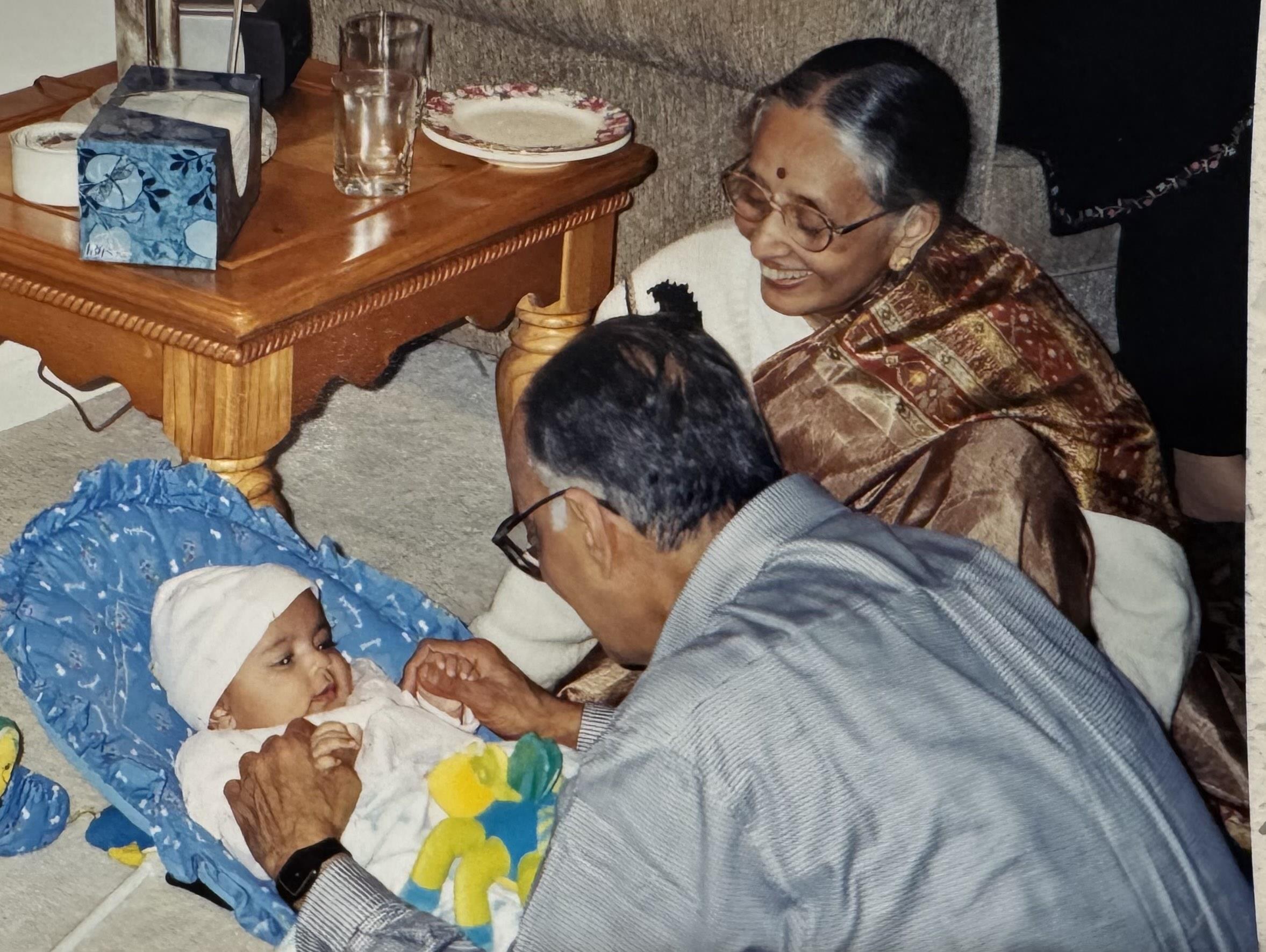 A baby plays with grandparents in a living room filled with love and joy during the day.