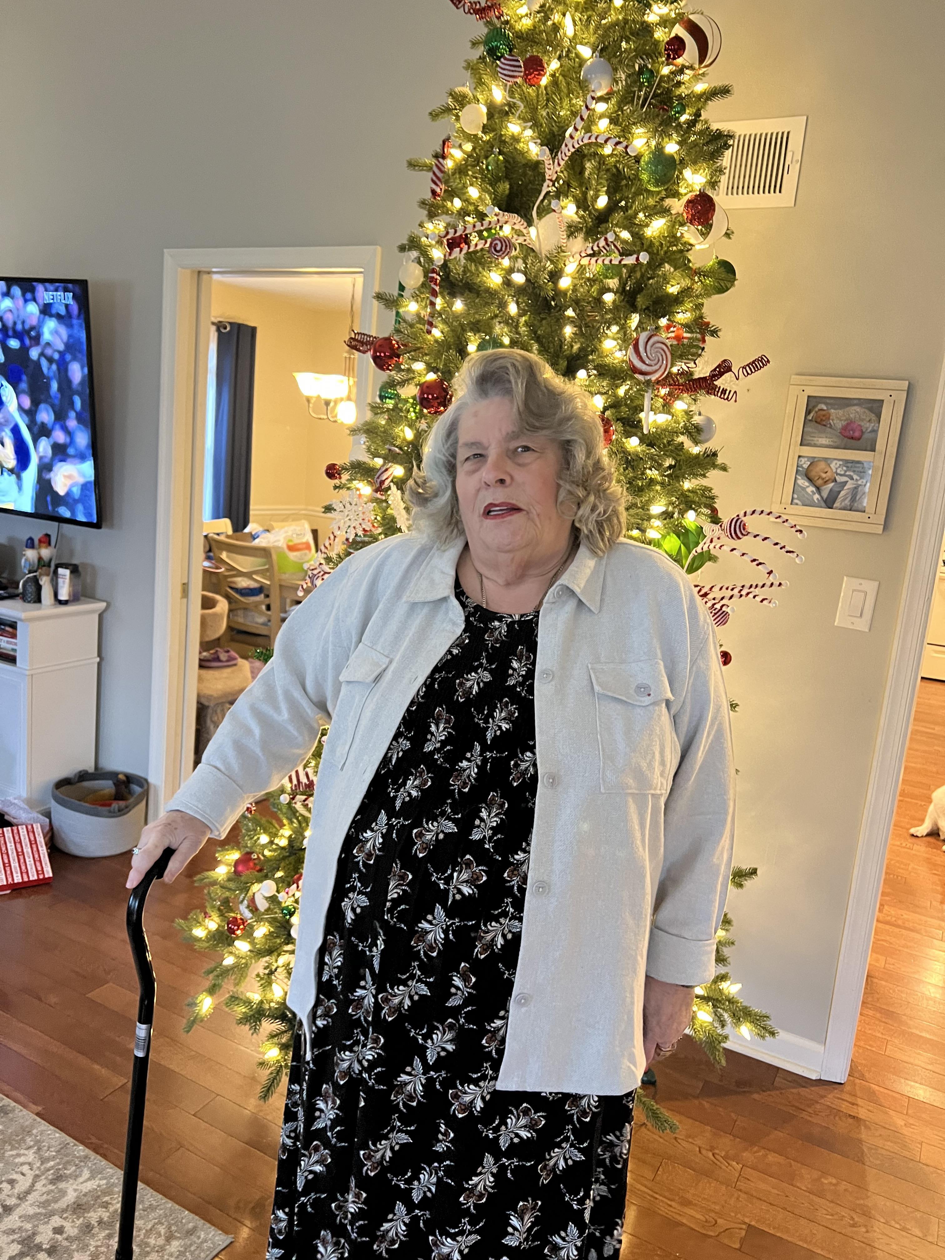 A woman stands next to a decorated Christmas tree in a cozy living room.