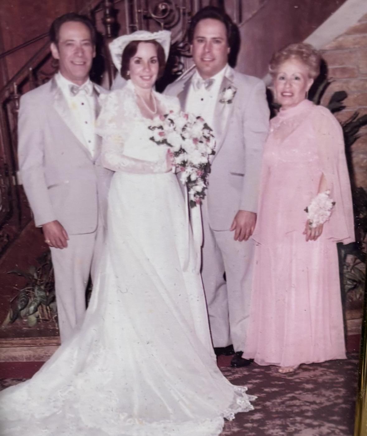 Two couples stand together at a wedding, showcasing formal attire and floral arrangements.
