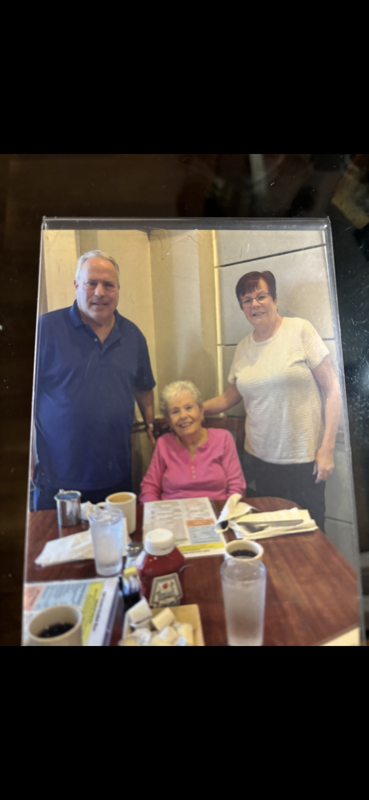 Three people gather at a table, sharing food and drinks while smiling at each other.