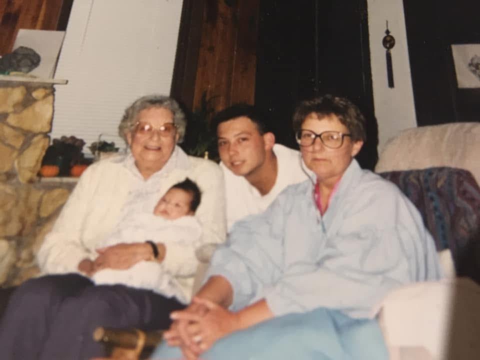 Four people are sitting on a sofa, enjoying time together and holding a baby in their arms.
