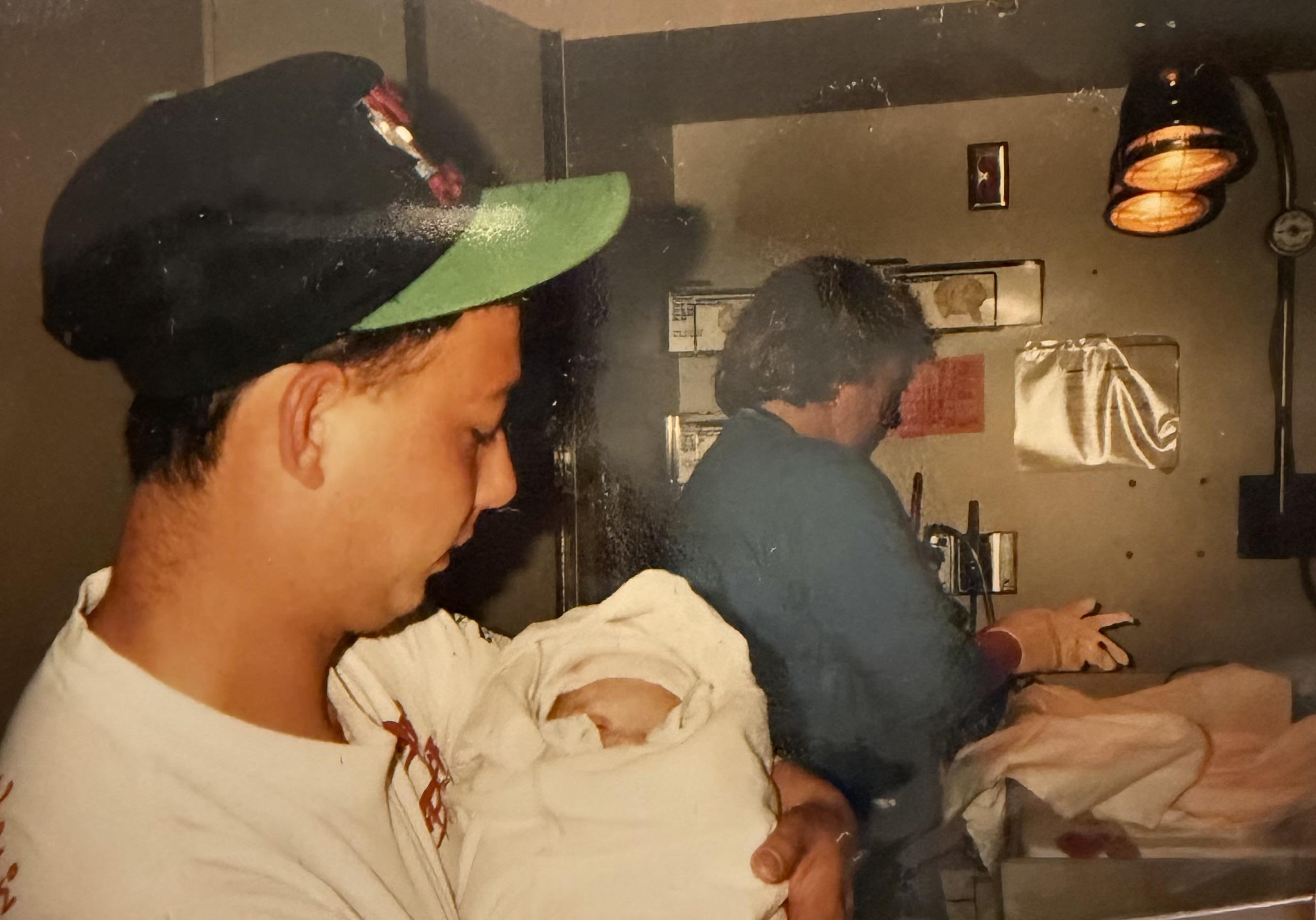 A father gently holds his newborn baby wrapped in a blanket in a hospital room.