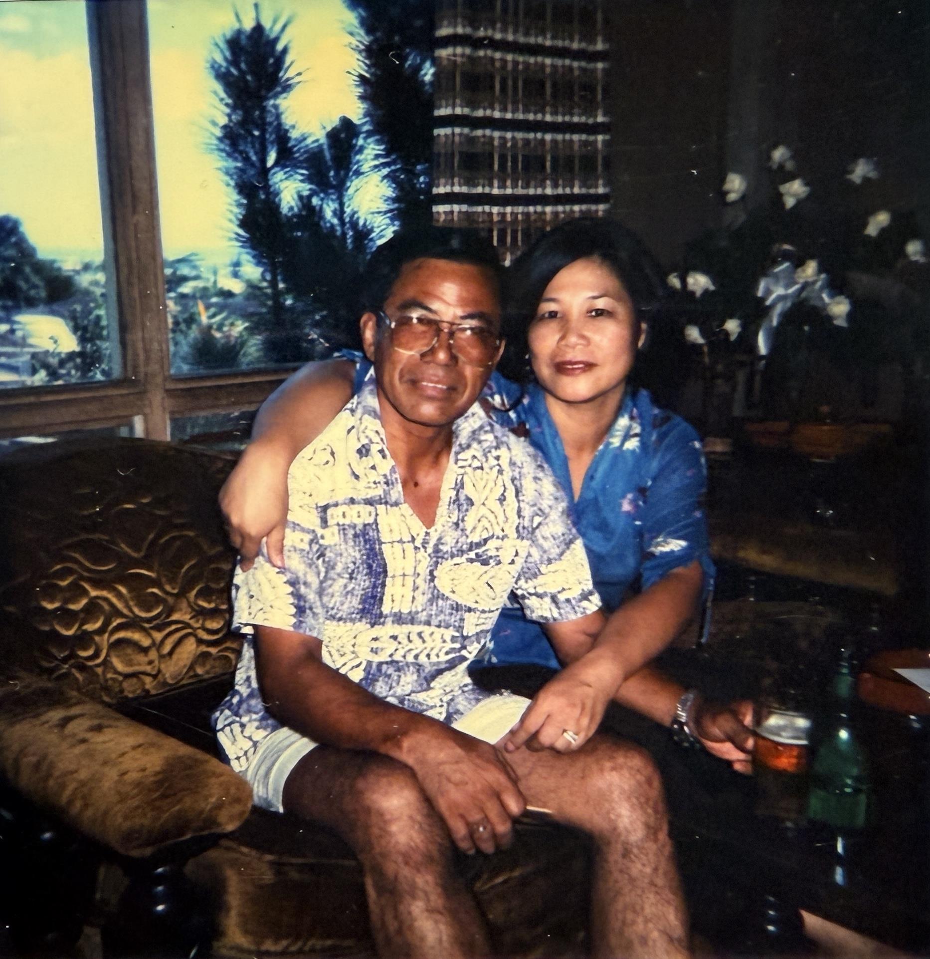 A man and woman are sitting close on a sofa in a living room. They are smiling and relaxed.