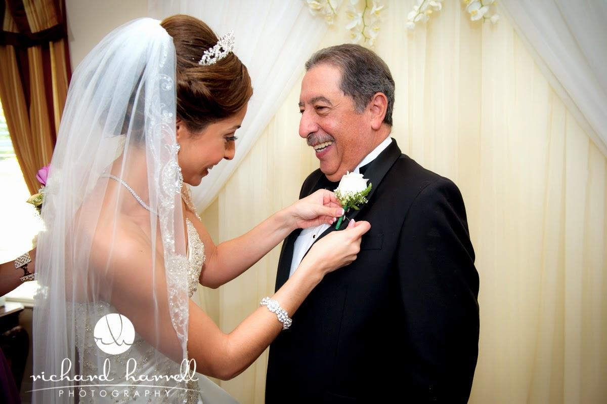 A bride attaches a boutonniere to her father's tuxedo in a venue before the ceremony starts.
