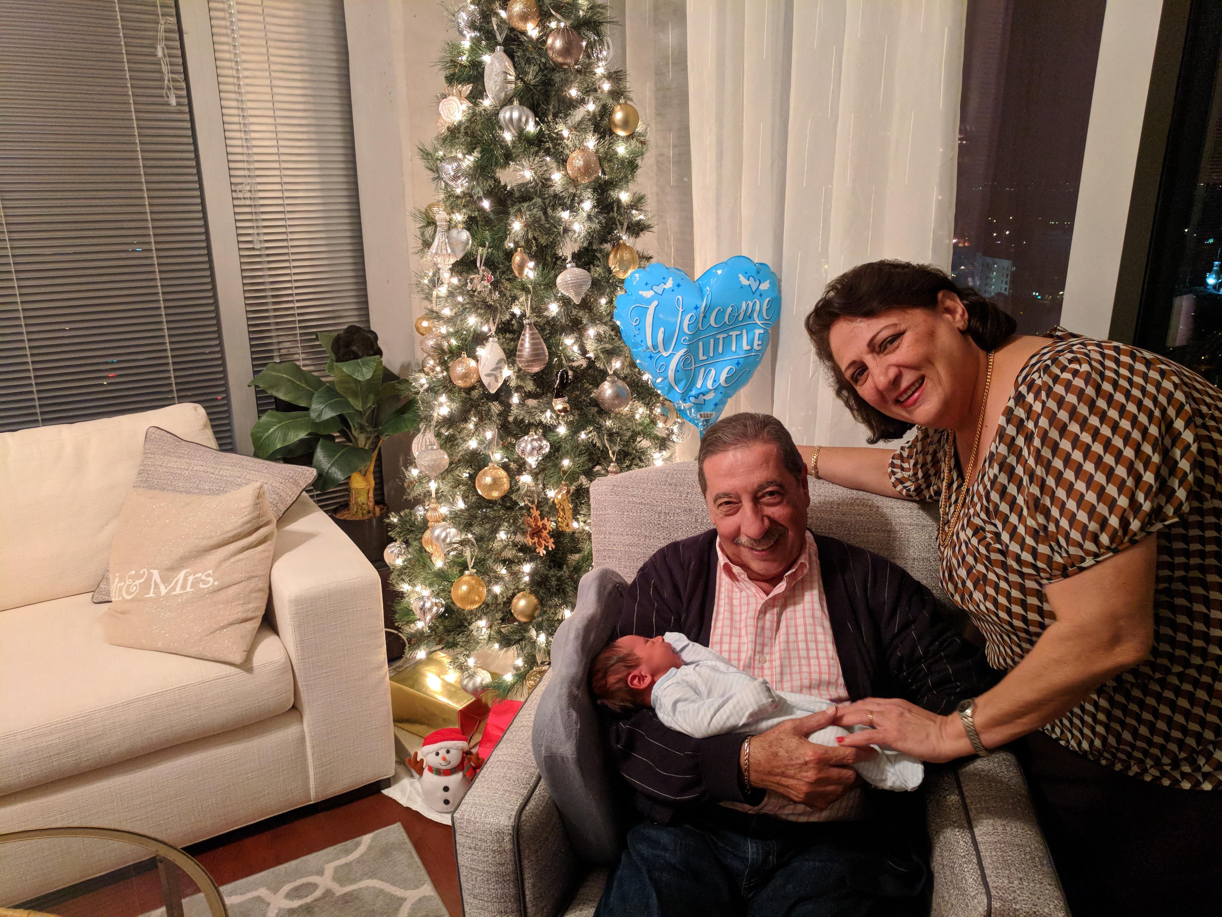 A family enjoys time together with a newborn near a decorated Christmas tree in the evening.