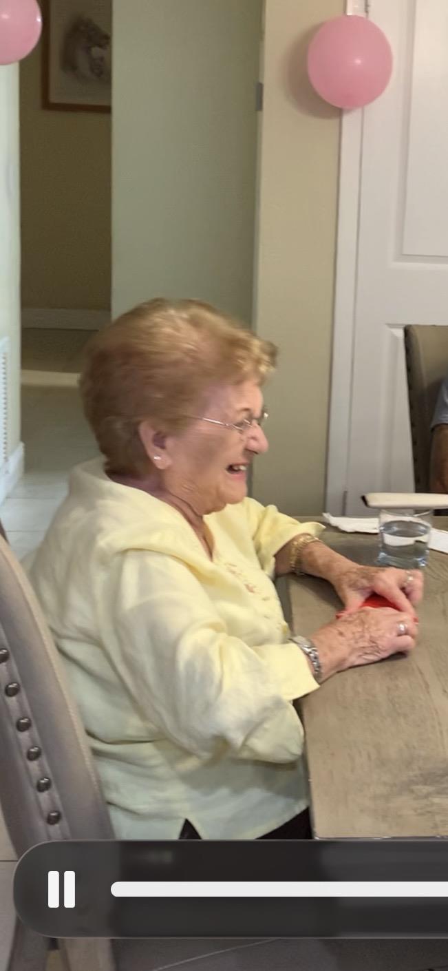 An elderly woman smiles and enjoys playing cards with friends at a dining table.