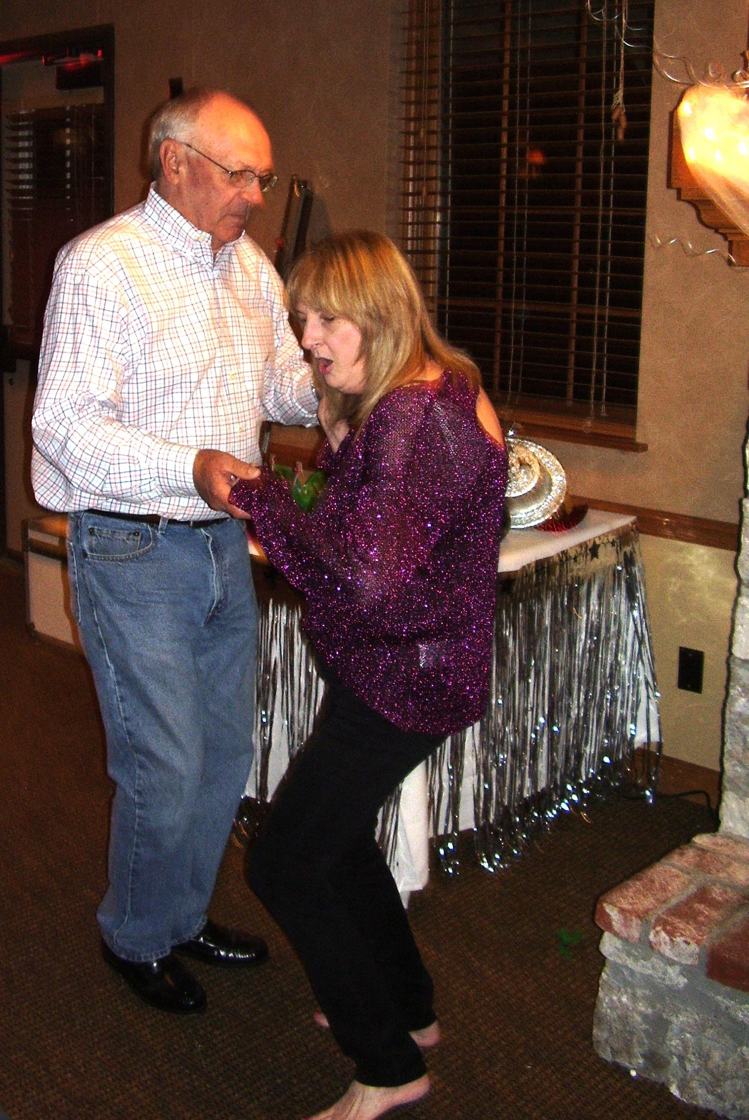 Two people dance closely in a room filled with decorations while others celebrate nearby.