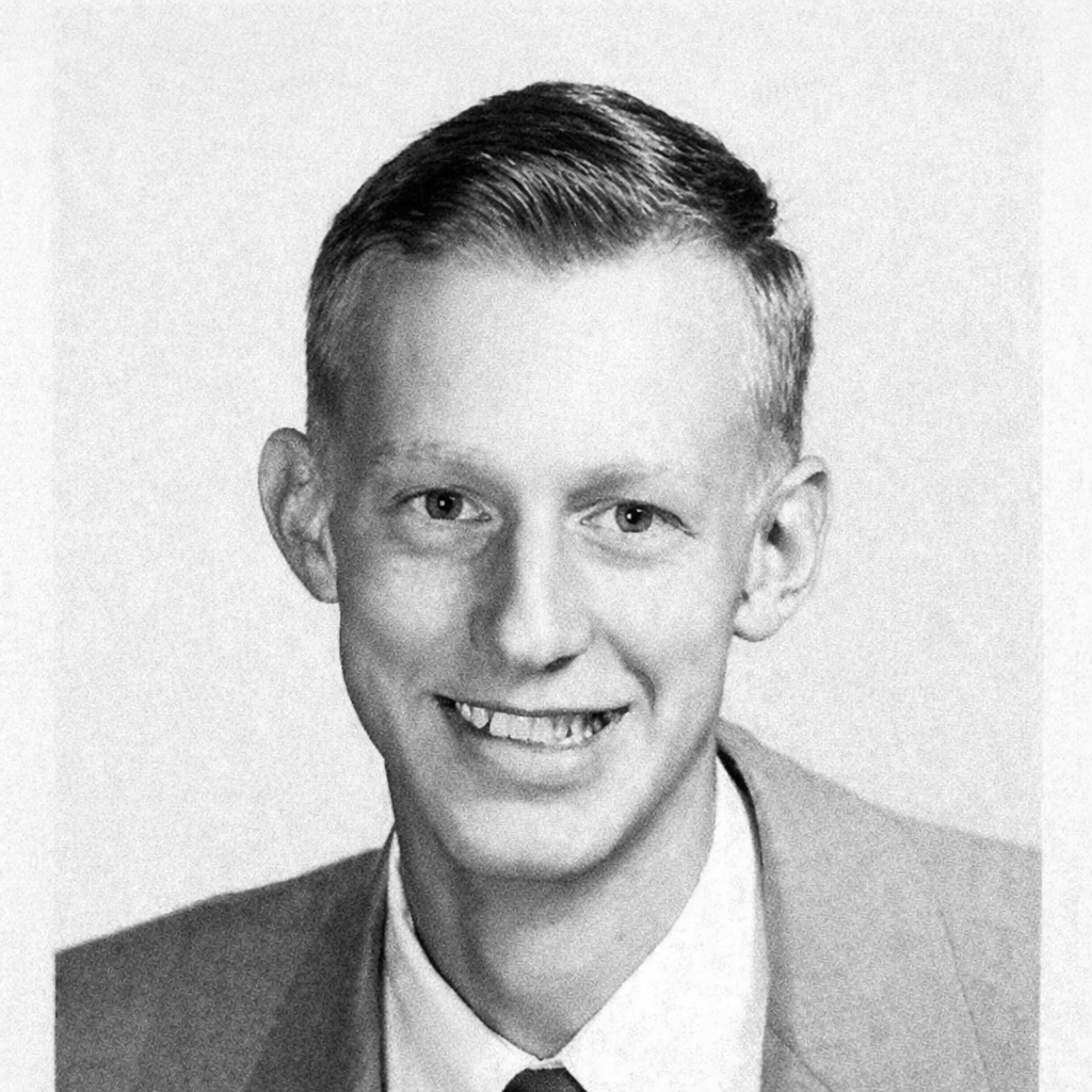 Man poses for a studio portrait with a smile, showing short hair and wearing a suit and tie.