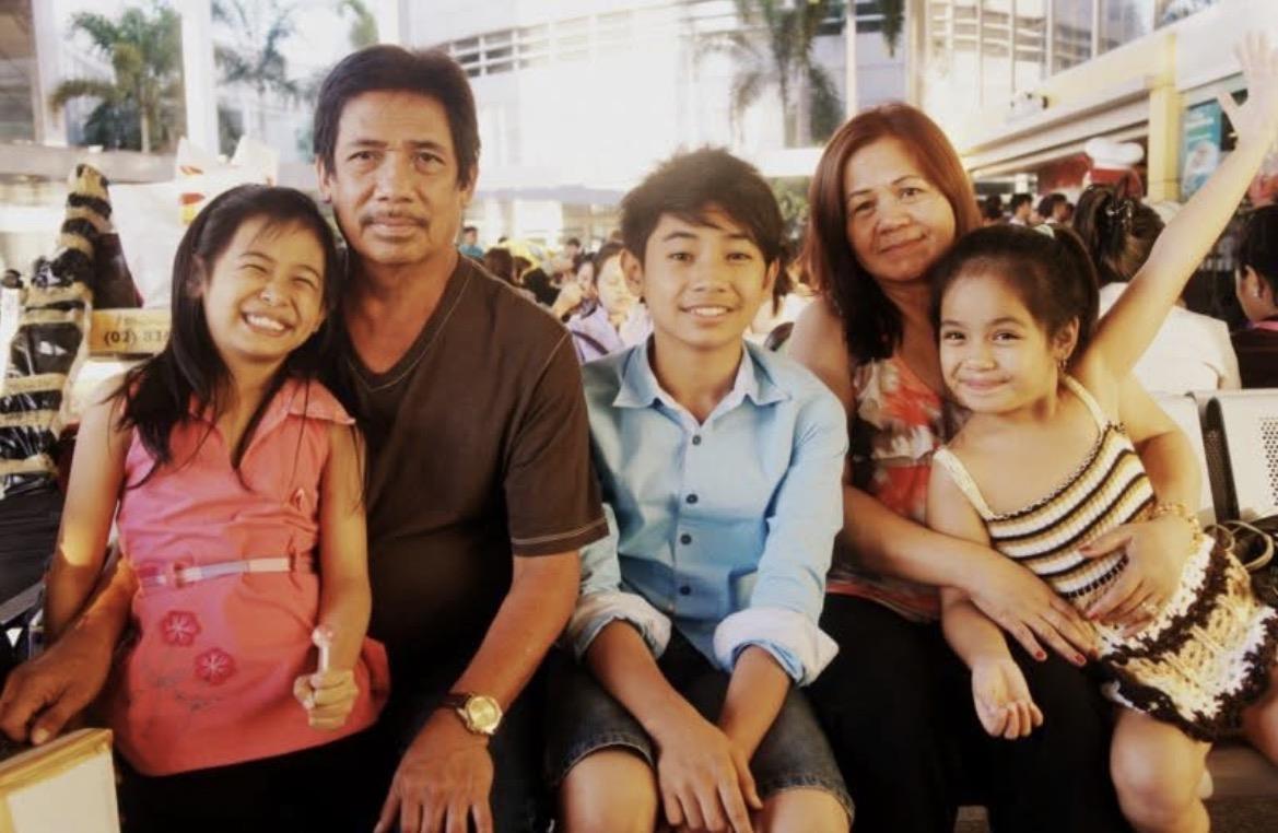 Group of five people sit together and smile at a busy location while enjoying the day.